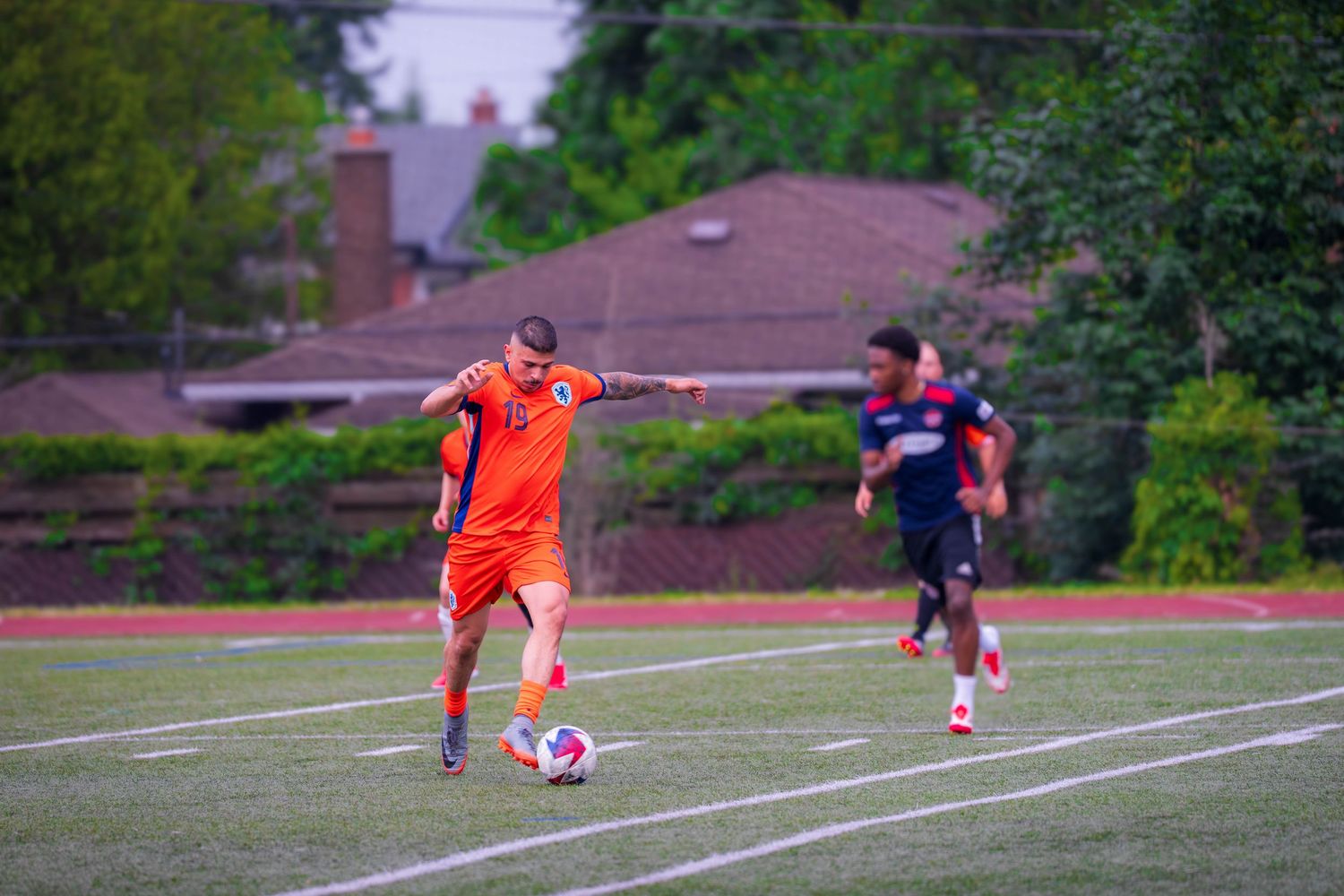 Soccer players compete on a grass field with one wearing an orange jersey during a match.