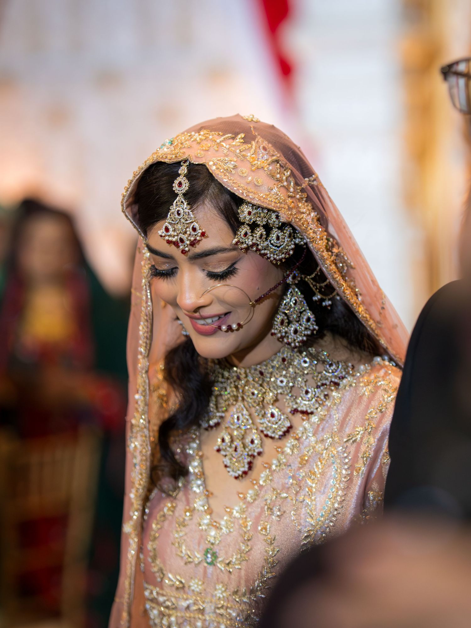 Close-up of bride wearing ornate pink lehenga with intricate jewelry and traditional South Asian bridal makeup.