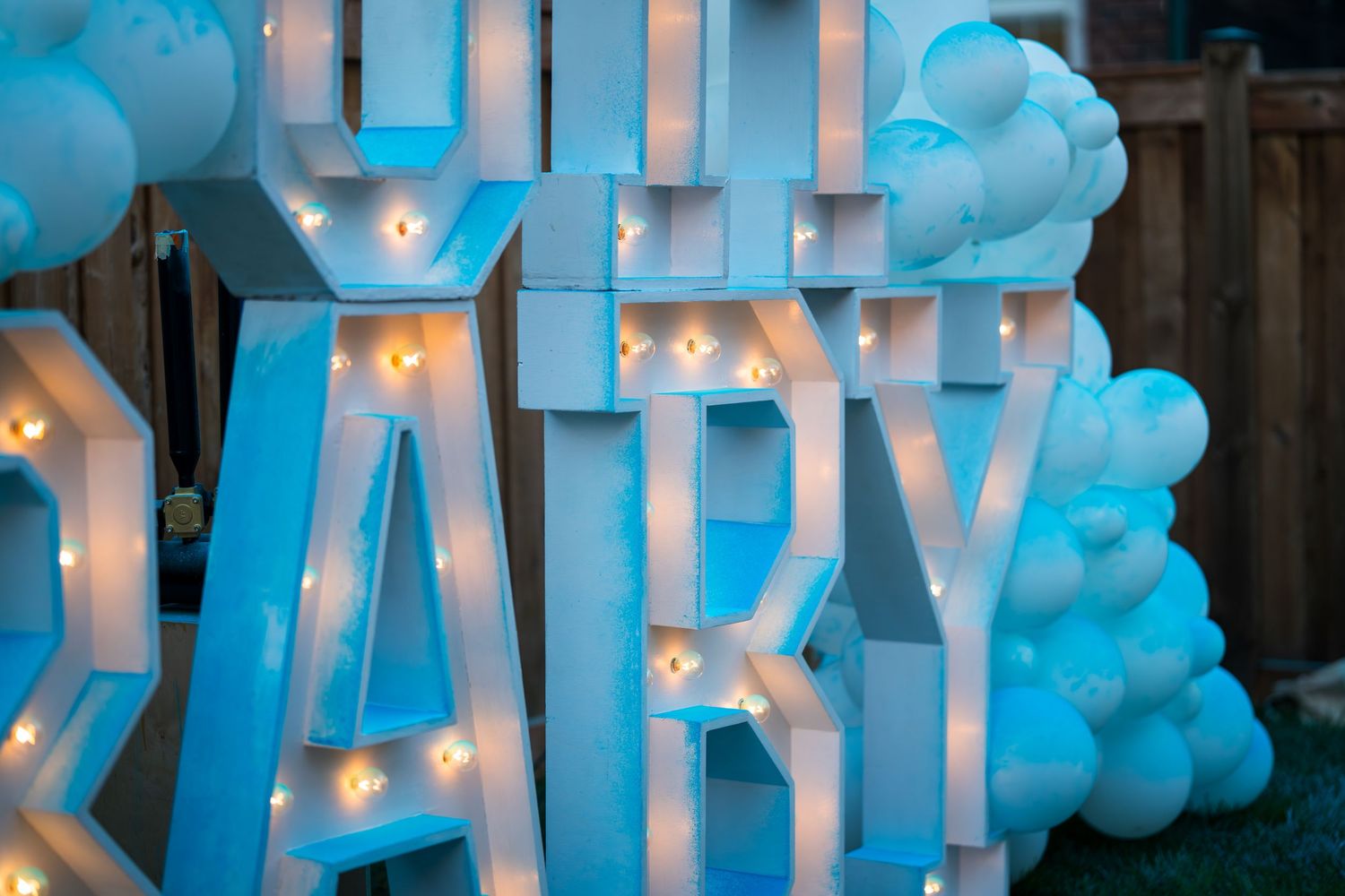 Illuminated OH BABY marquee letters surrounded by blue and white balloon decorations at night.
