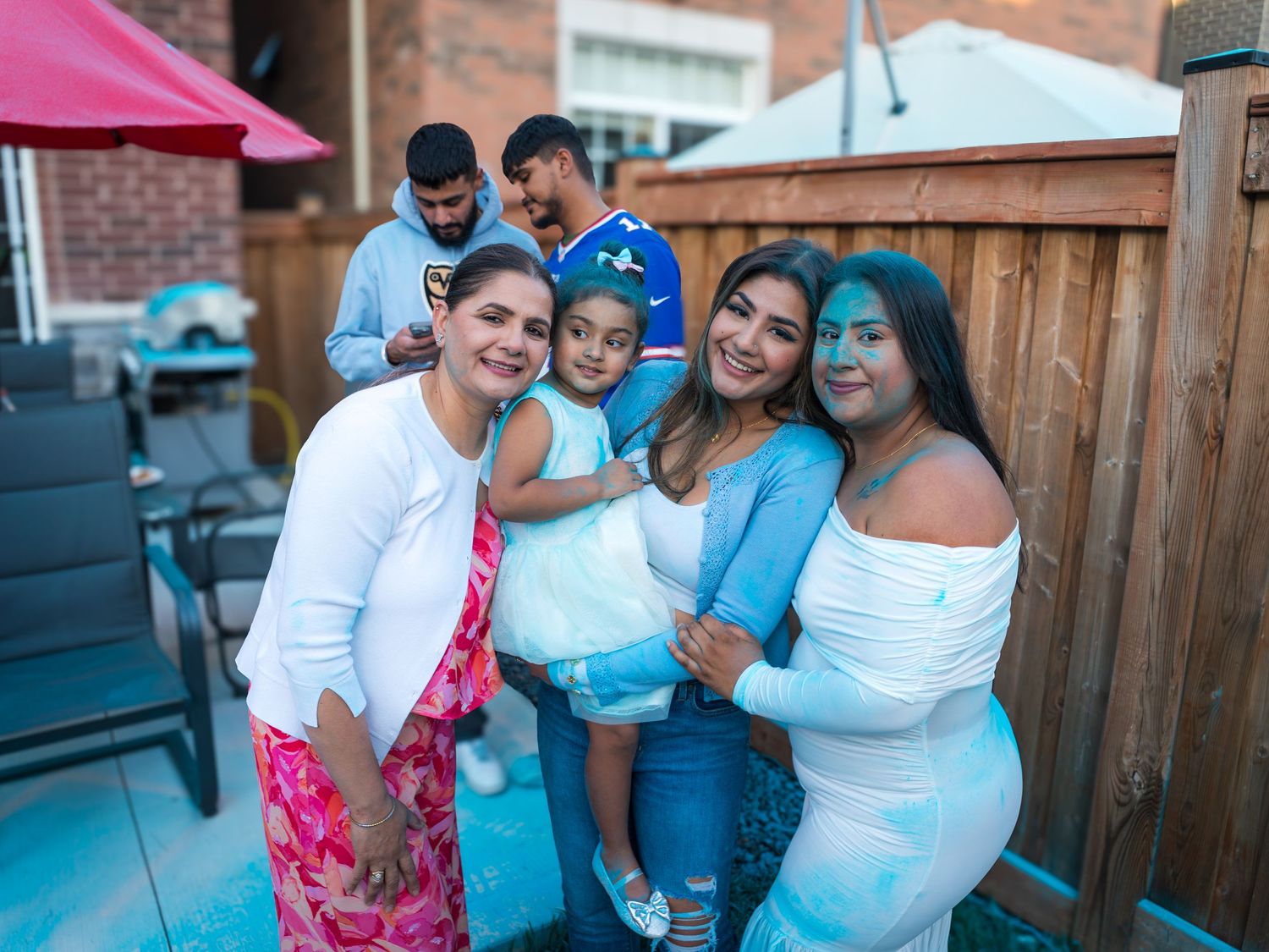 Joyful family members covered in blue powder celebrate a boy gender reveal party outdoors.