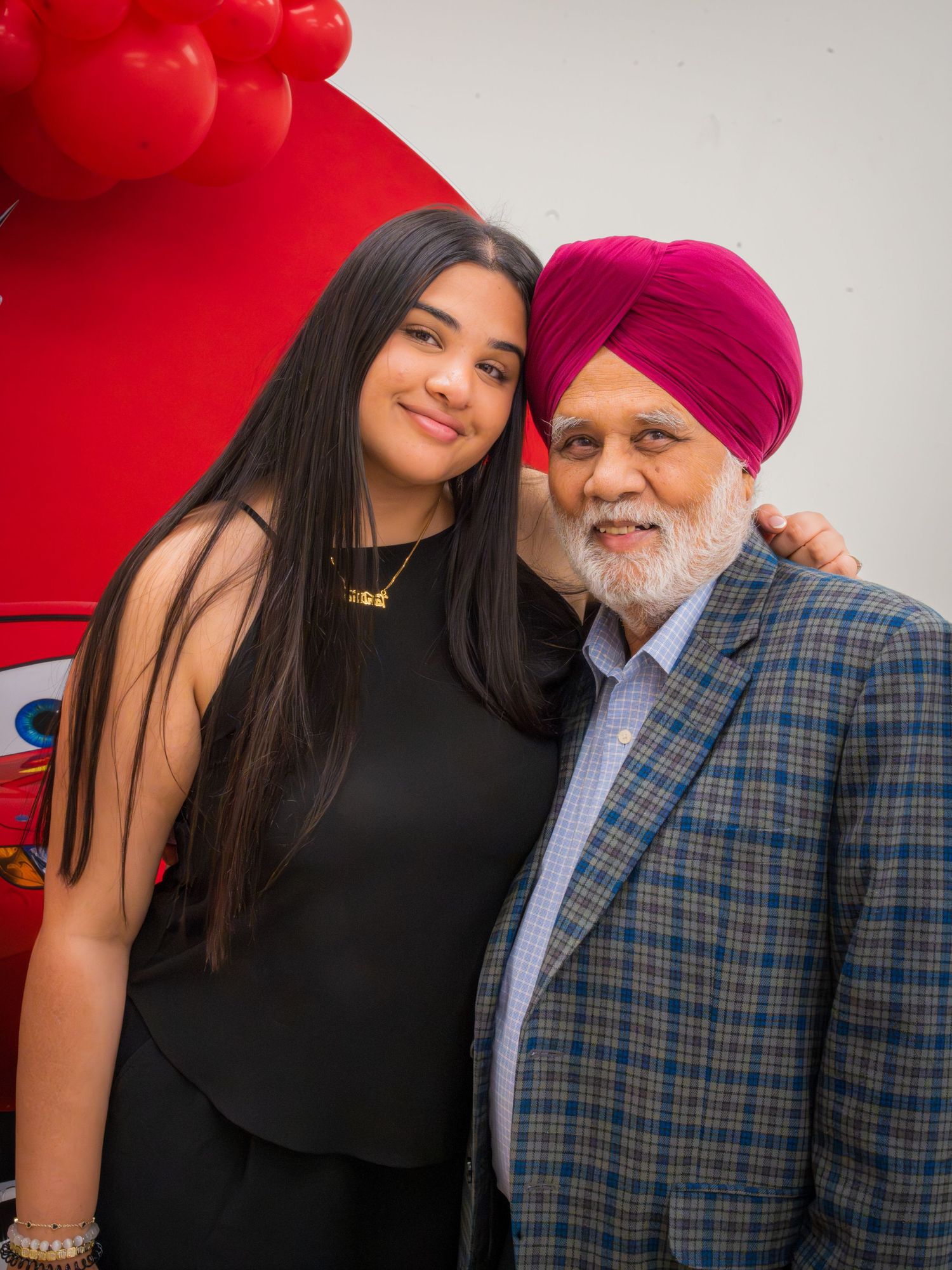 Young woman in black dress posing with an elderly Sikh man in a pink turban.