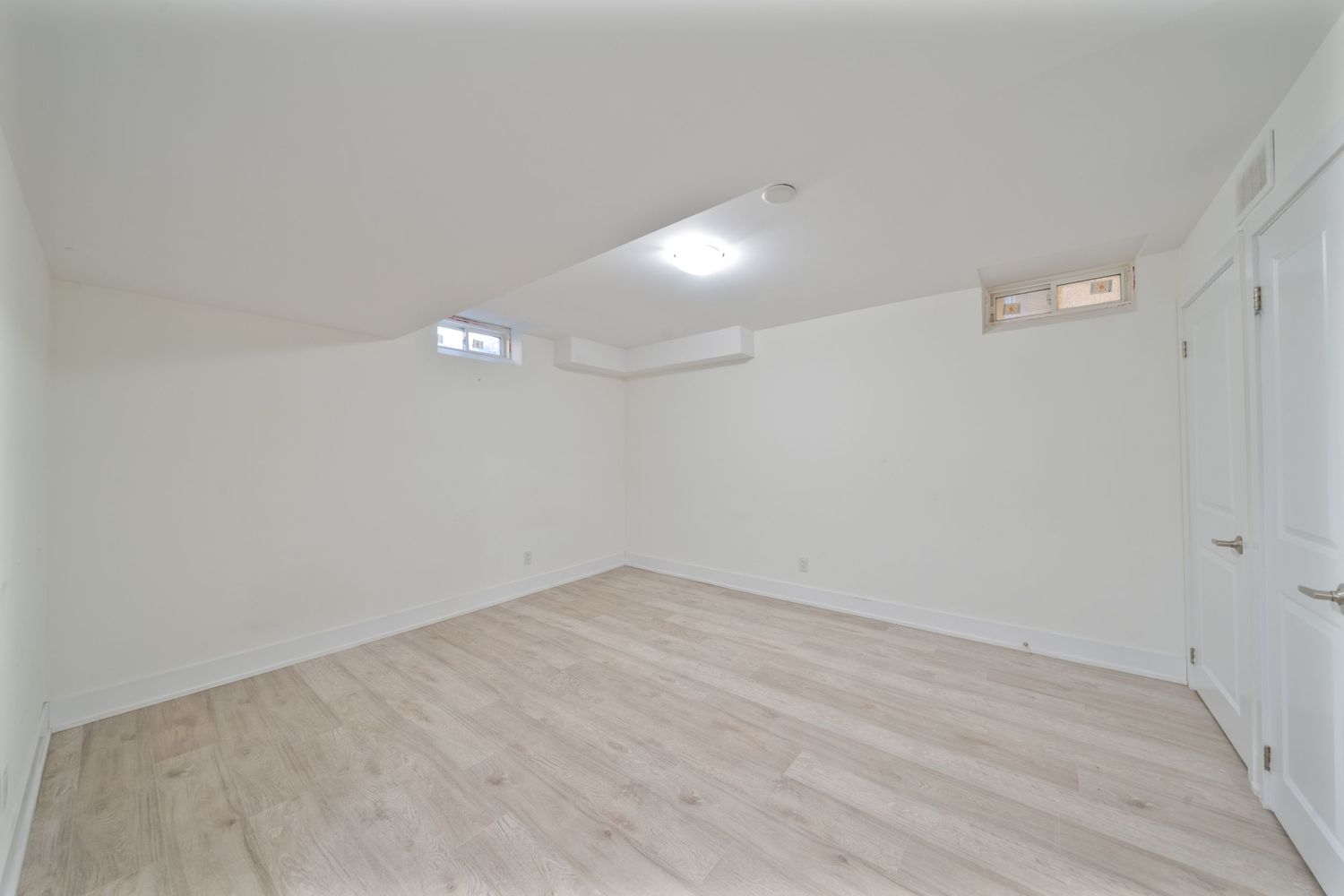 Empty room interior with white walls, hardwood flooring, and recessed lighting in a modern minimalist design.