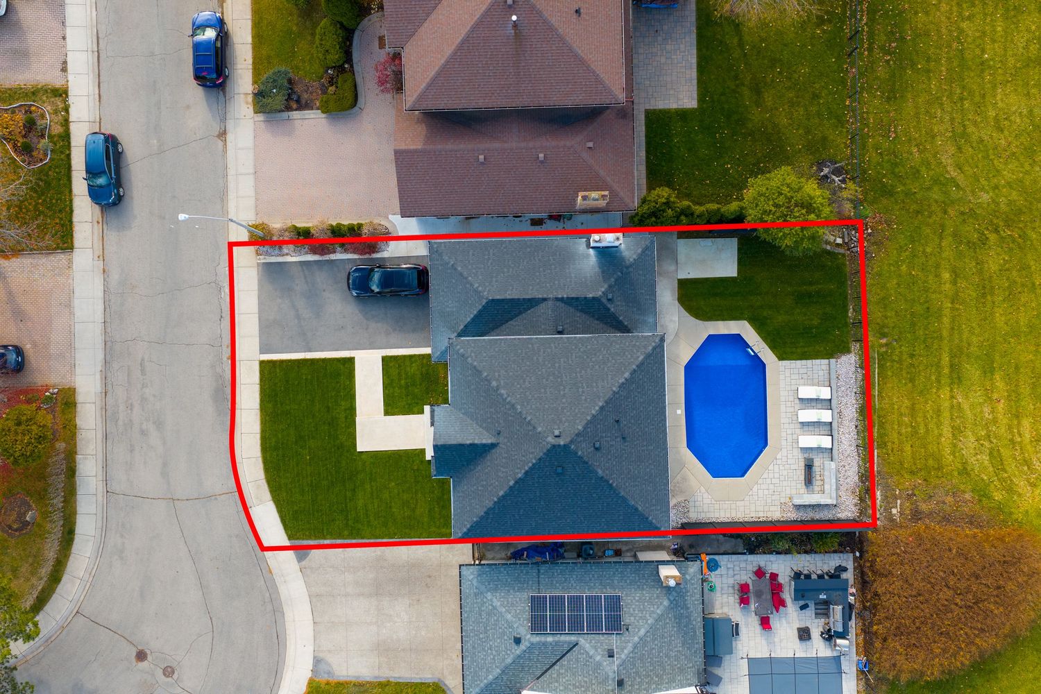 Aerial view of a residential property with blue roof, swimming pool, and well-maintained lawn enclosed by red boundary lines.
