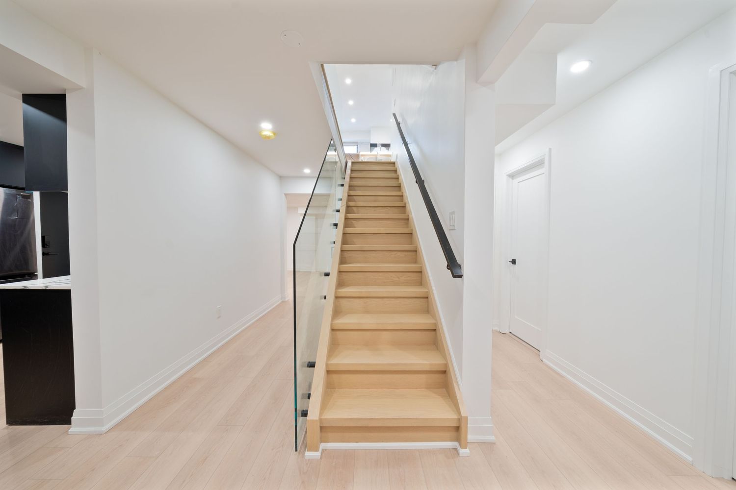 Modern white staircase with light wood treads and glass railing leads upward in a bright contemporary home interior.