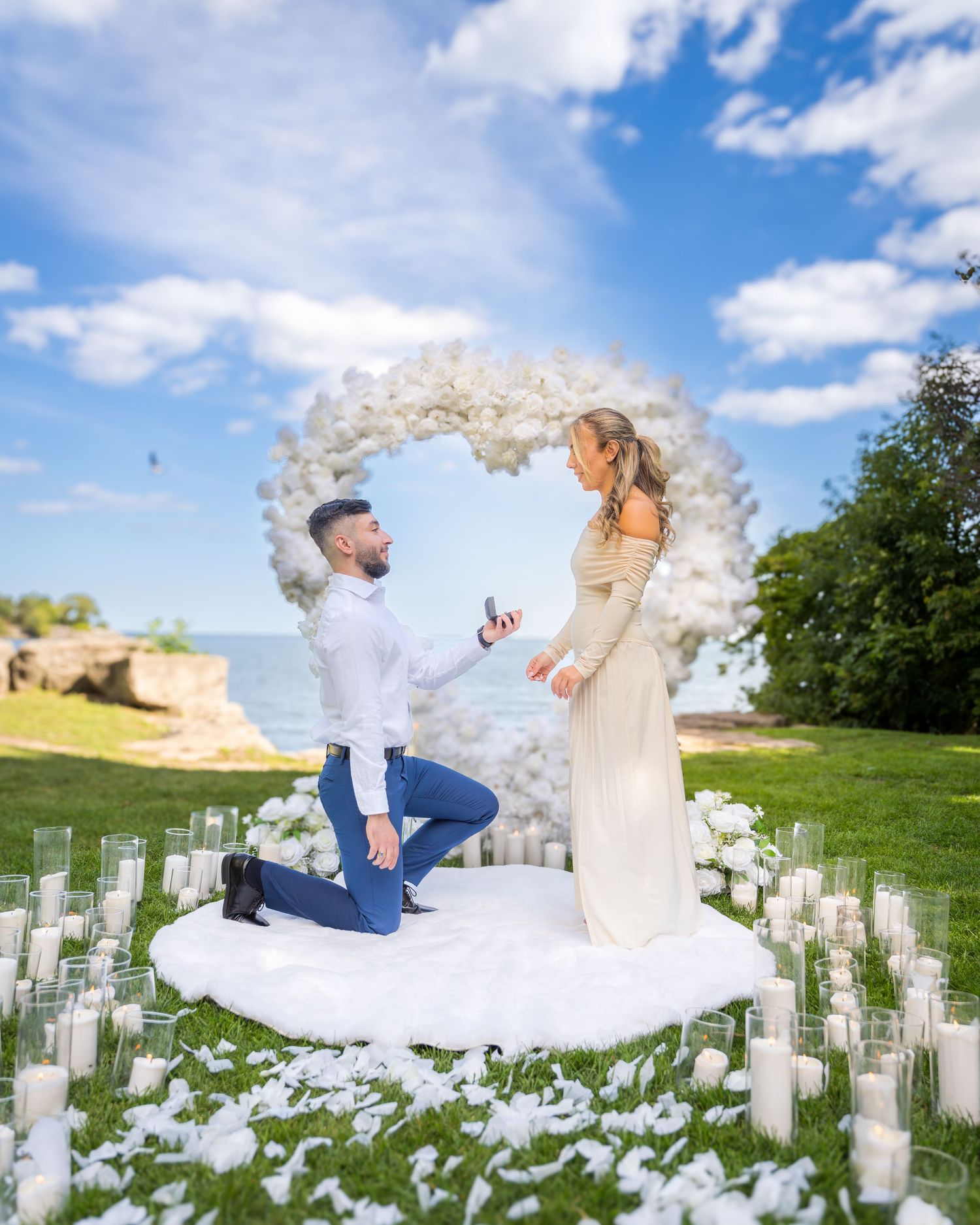 A romantic proposal scene with white floral decorations and a beautiful balloon arch under blue skies.