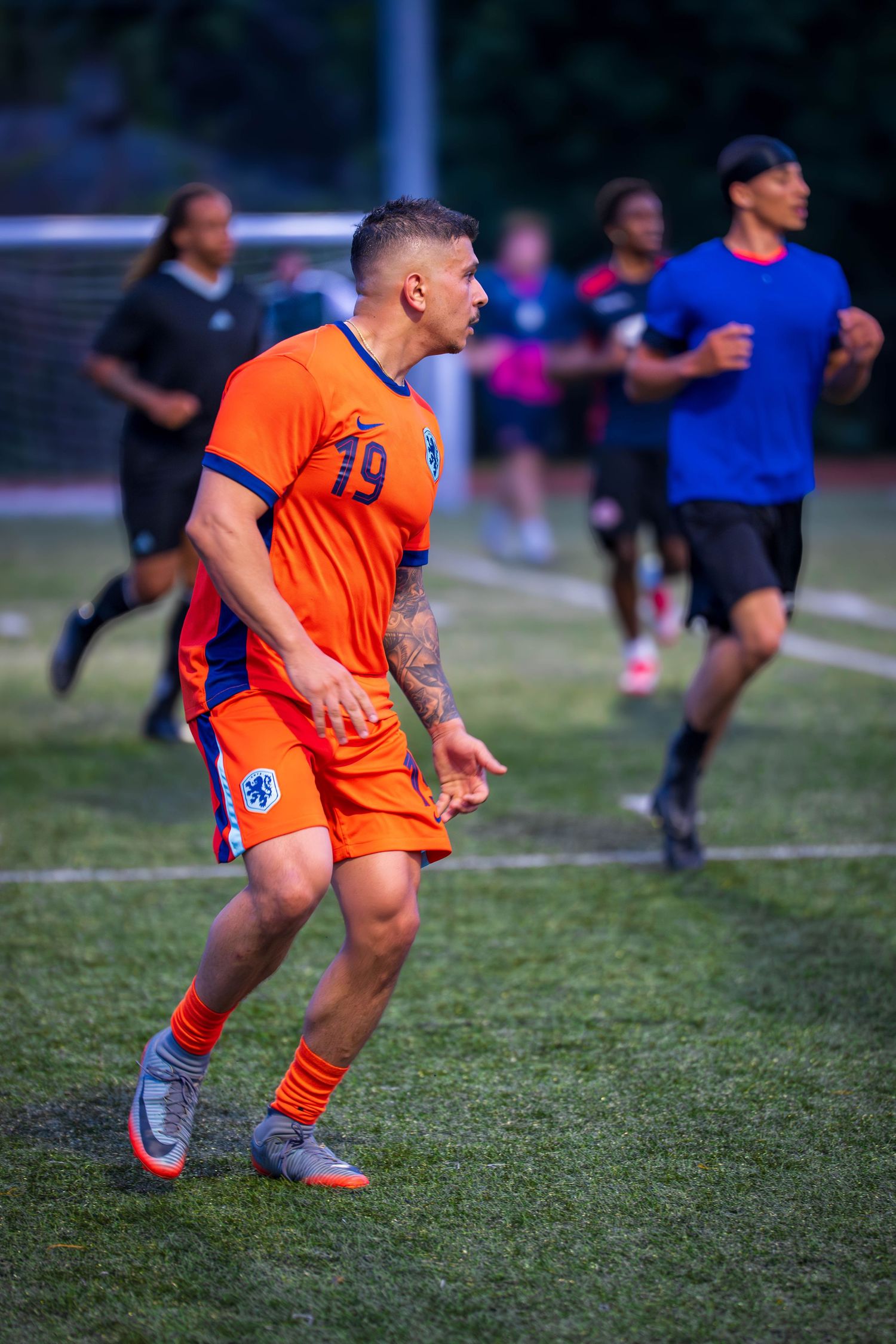 Athlete in bright orange uniform runs across soccer field during game.