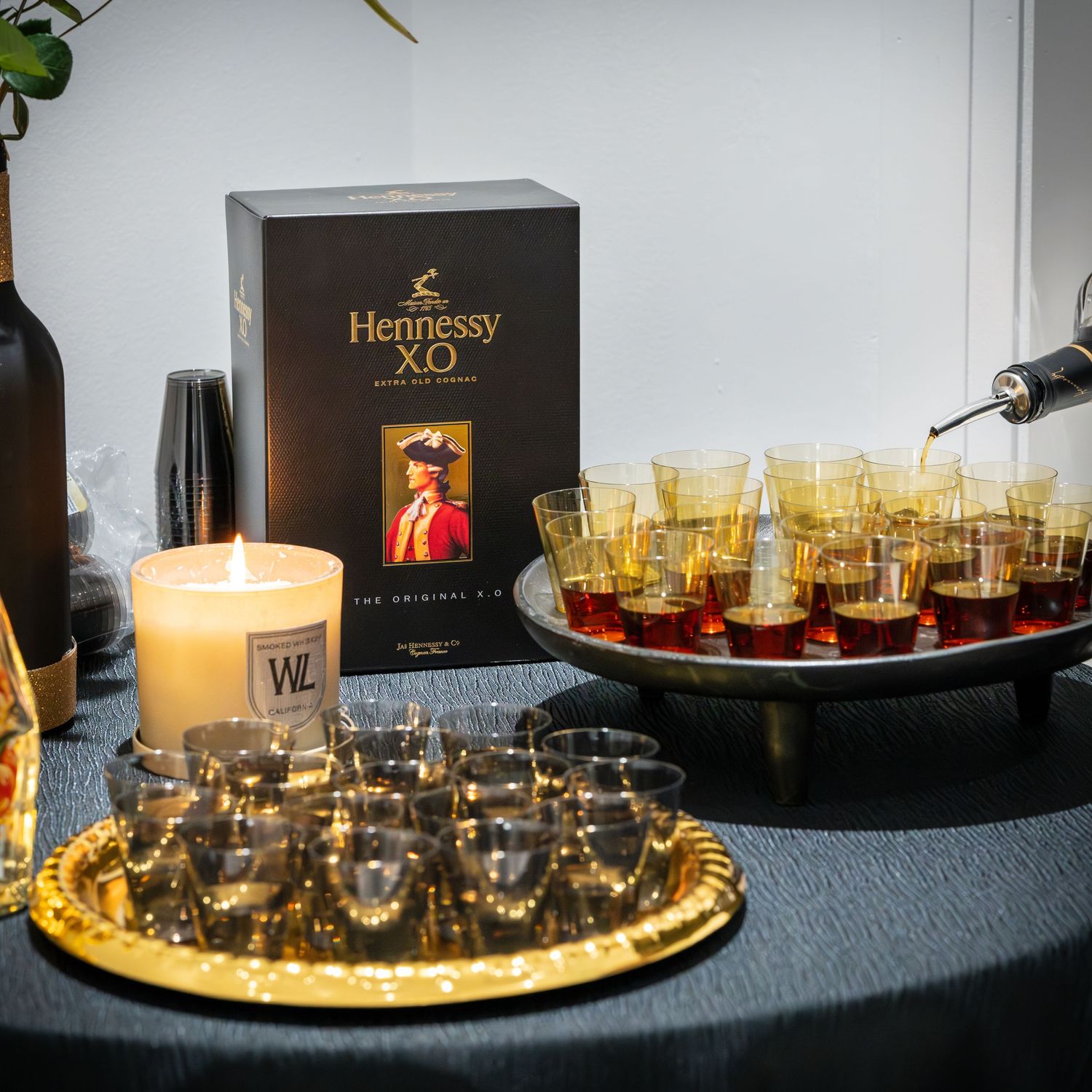Hennessy XO display with amber-filled shot glasses arranged on serving trays with a decorative candle.