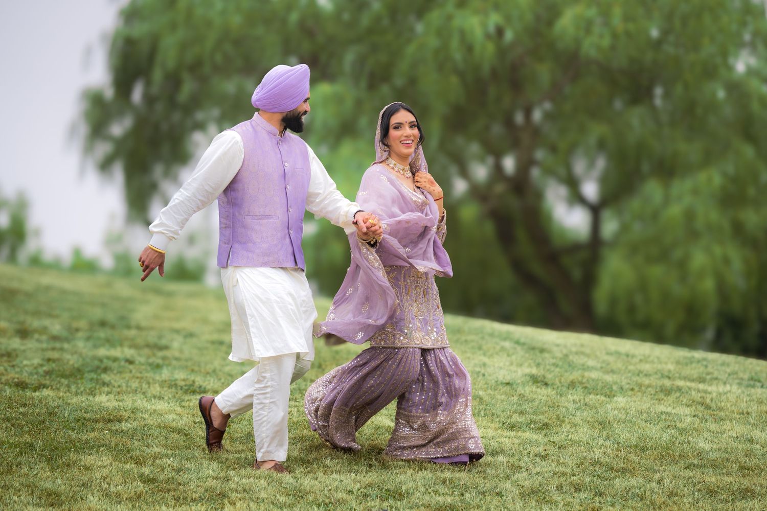 Couple in matching purple attire poses together on a grassy slope during an outdoor photoshoot.