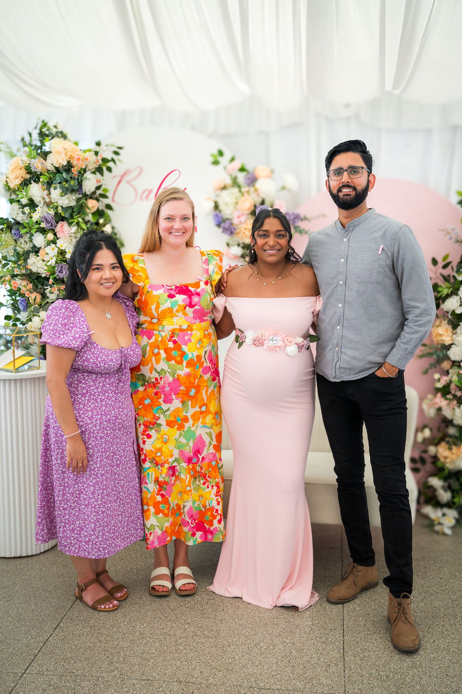 Guests in colorful dresses posing in small groups at a baby shower celebration.