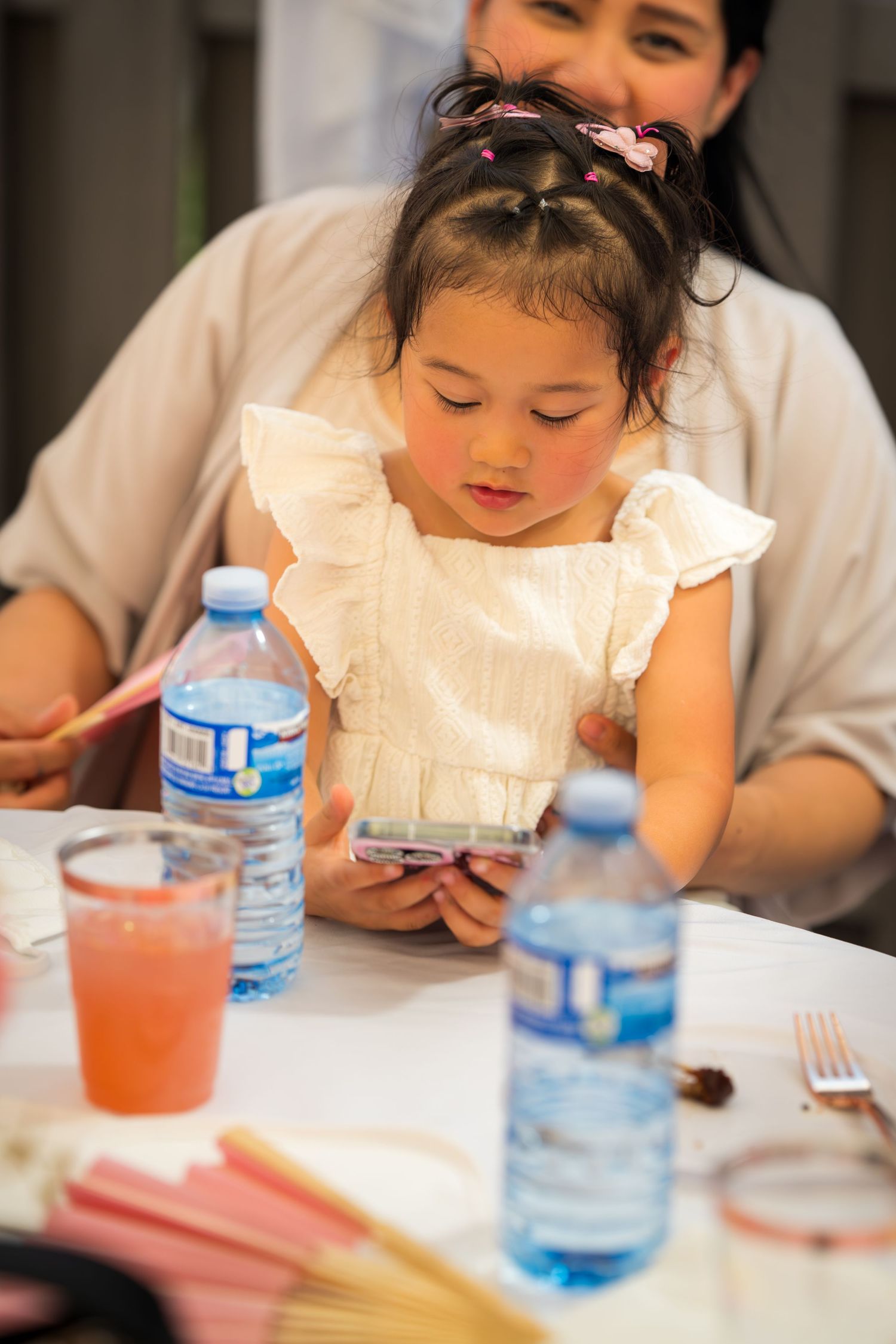 A child in a white dress sits at a table with beverages and place settings.