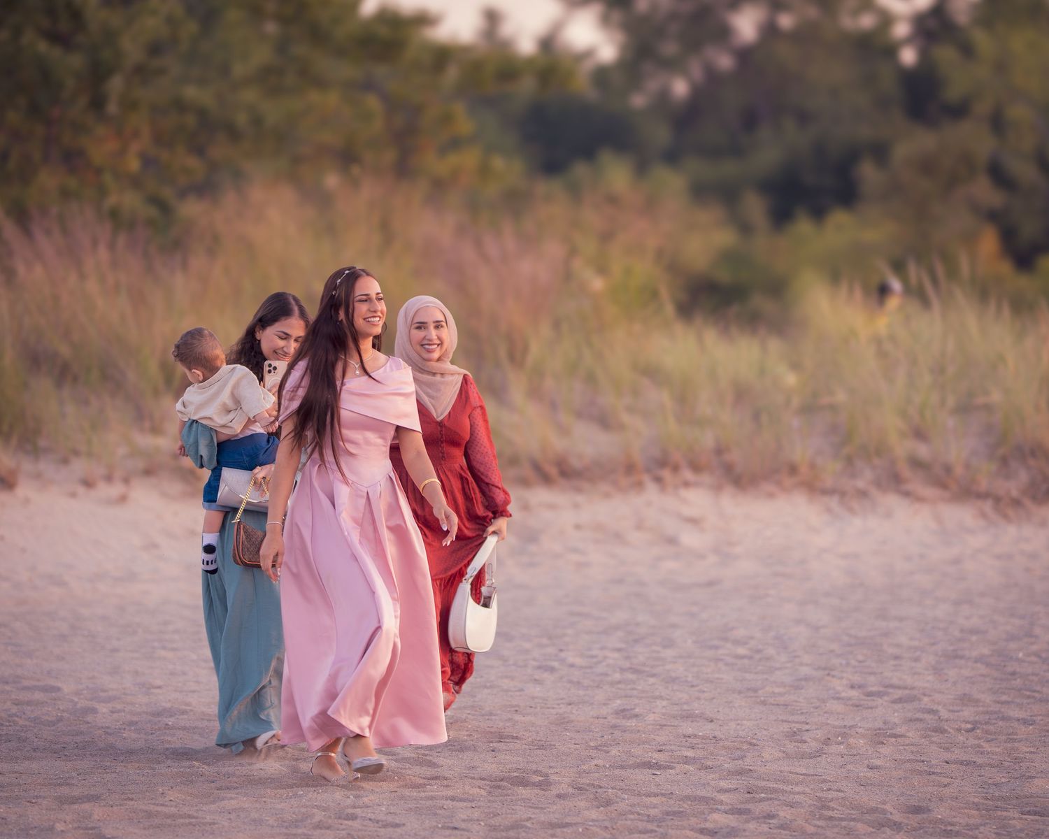 A group in coordinated pink and red outfits walks together on a sandy beach at sunset.