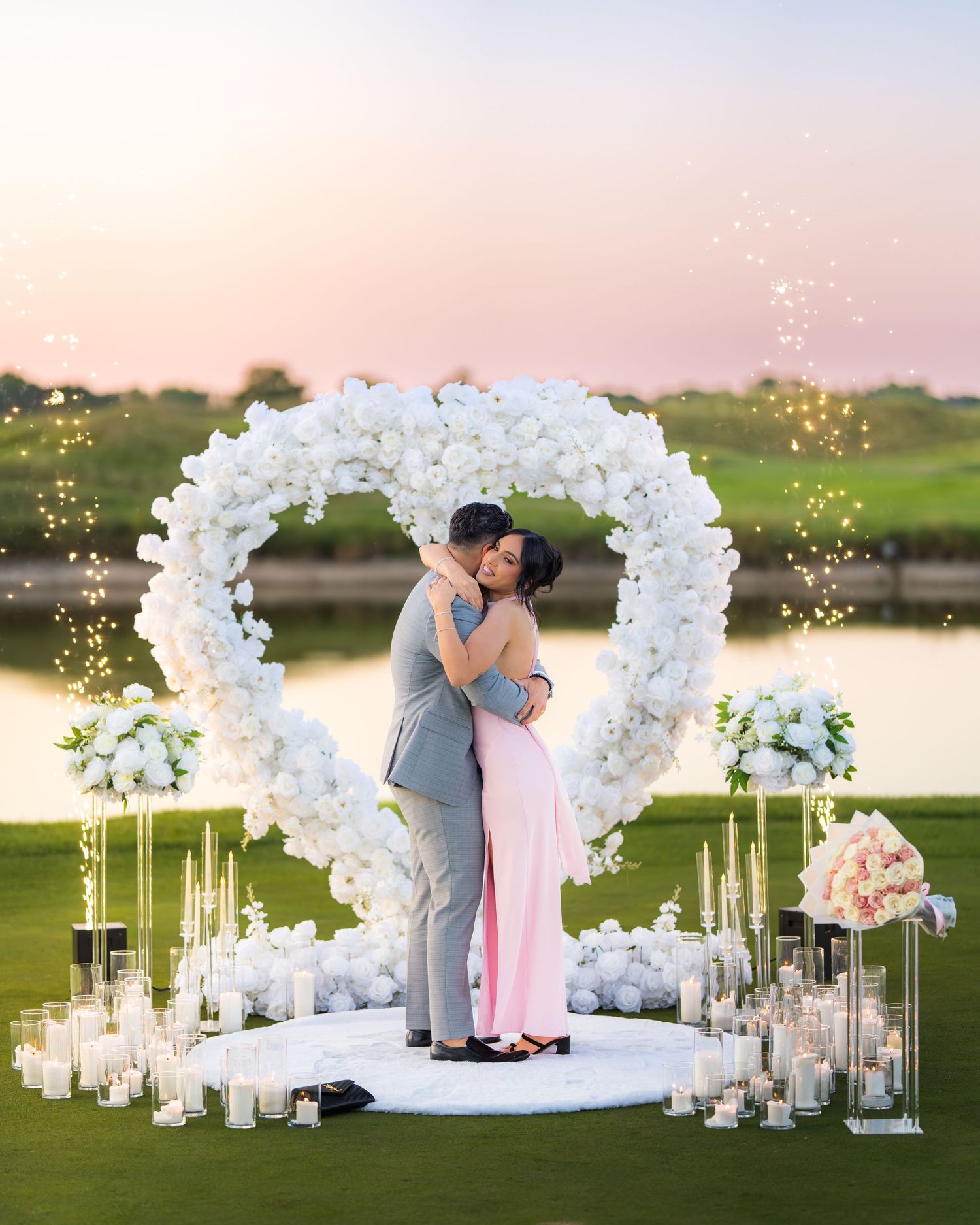 Romantic outdoor proposal scene with white flower arch and glowing candles.