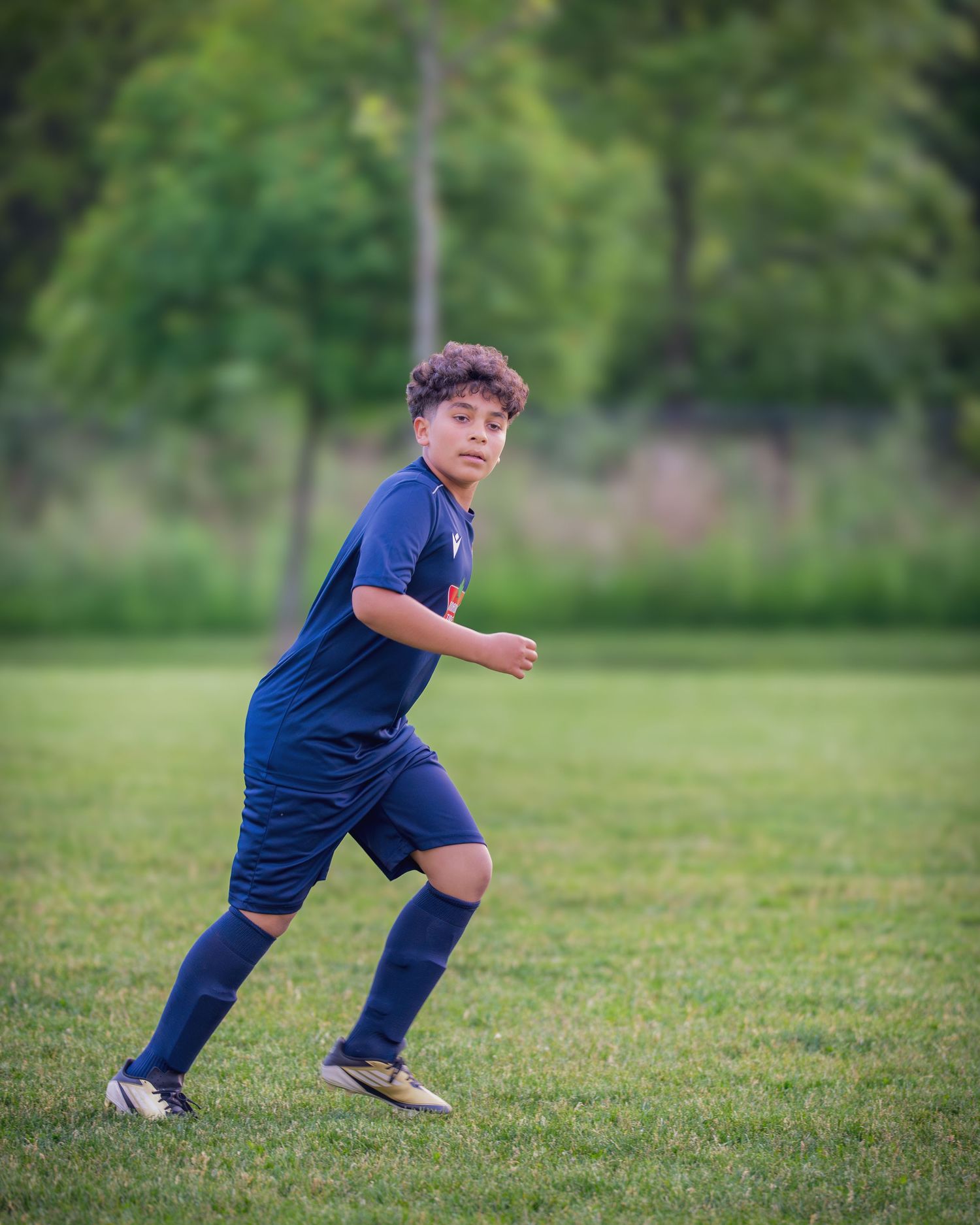 A person in a navy blue shirt and pants performs dynamic stretching exercises on a grassy field.