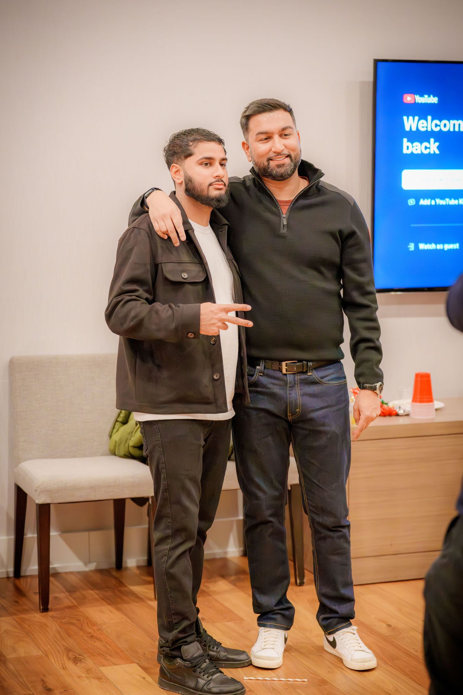 Two people standing together in casual attire at an indoor event with a TV screen visible.