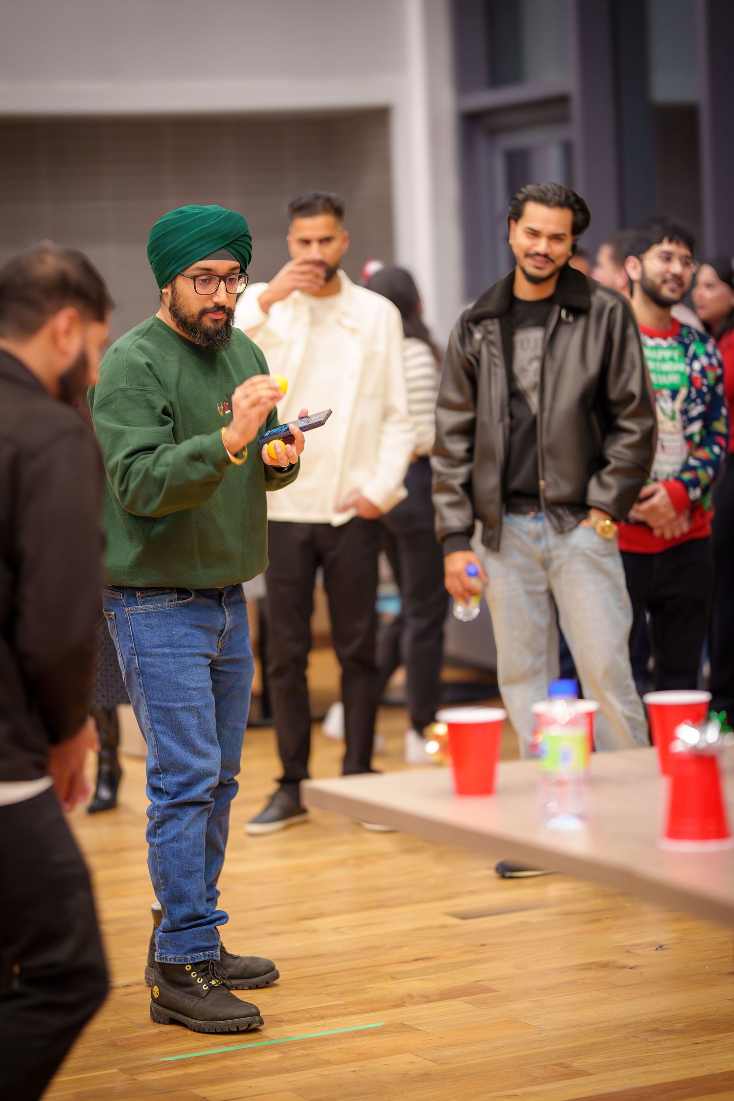 A group plays a party game with red cups on a wooden floor at an indoor gathering.