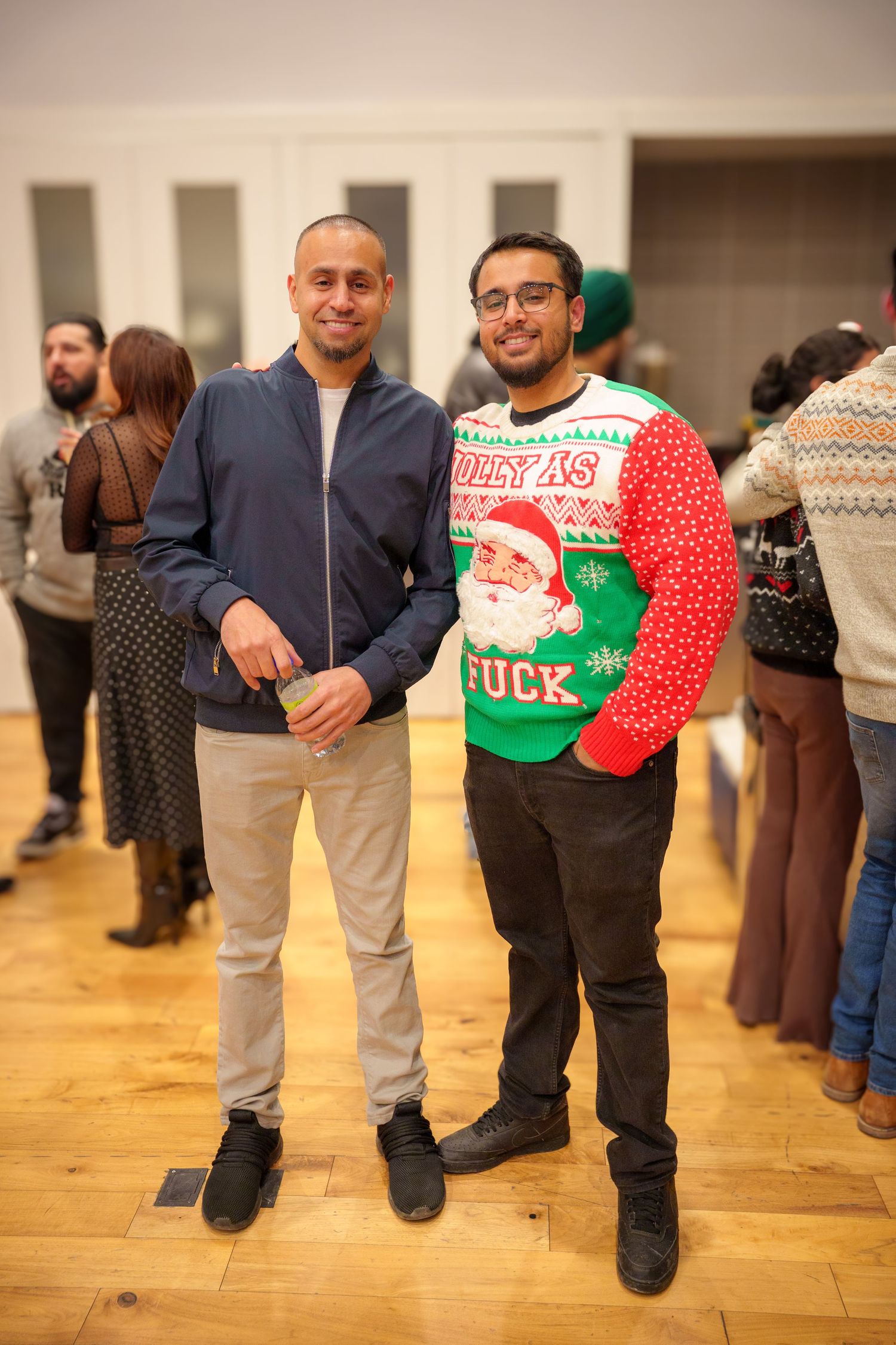 Group wearing festive holiday sweaters standing together at an indoor party with hardwood floors.