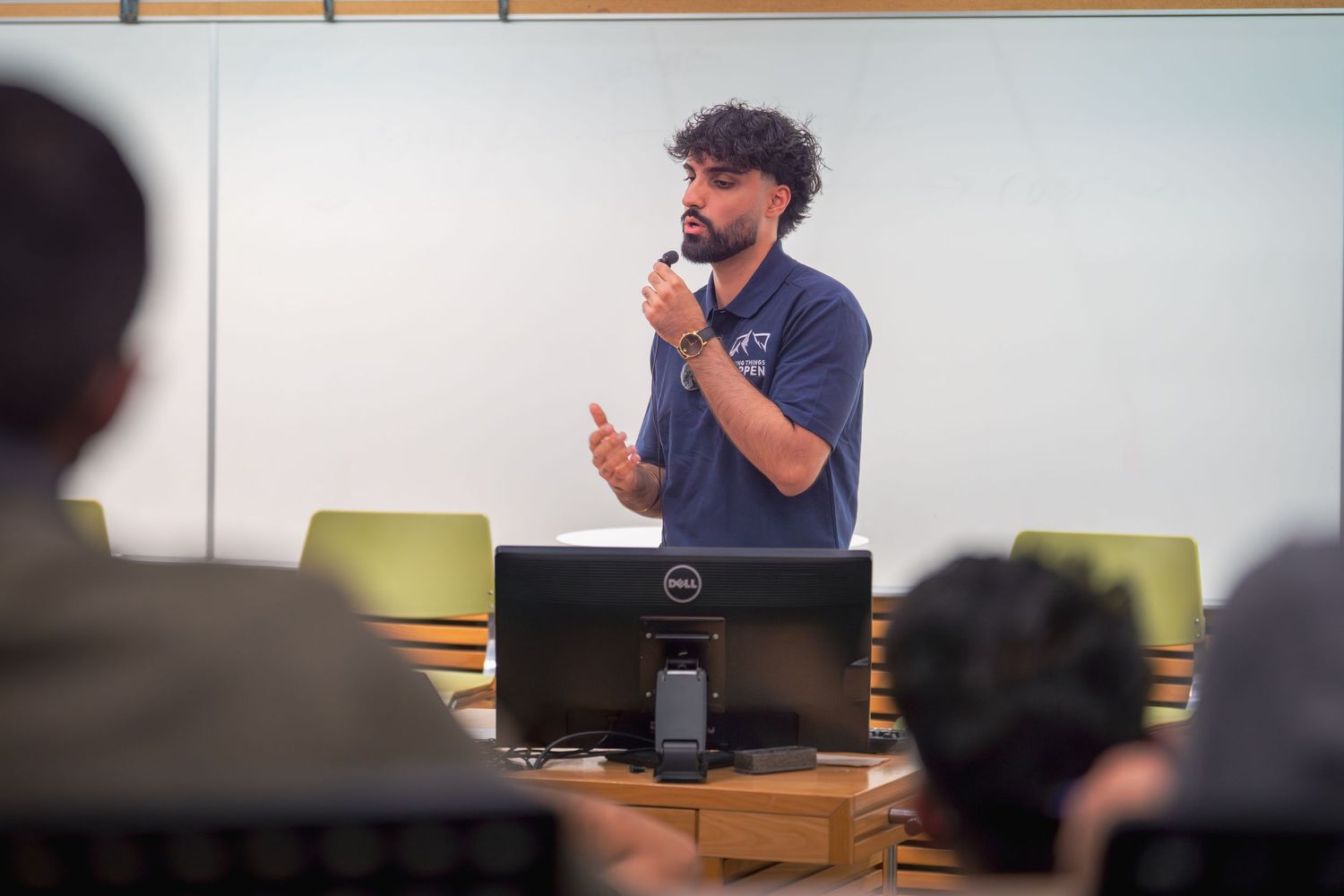 Presenter in navy blue shirt gesturing while speaking at podium with laptop.