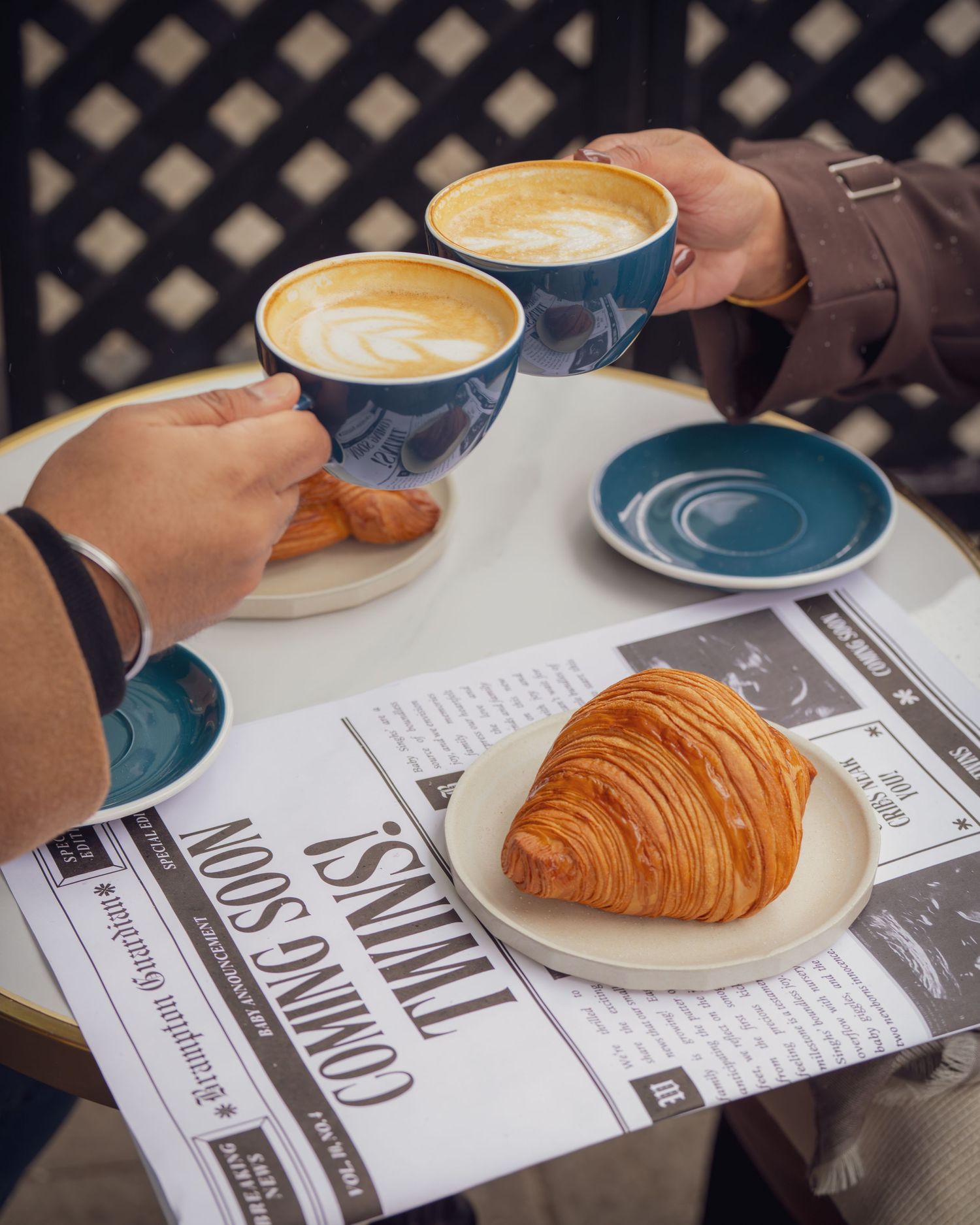 Coffee cups and croissants arranged on a table with a newspaper.