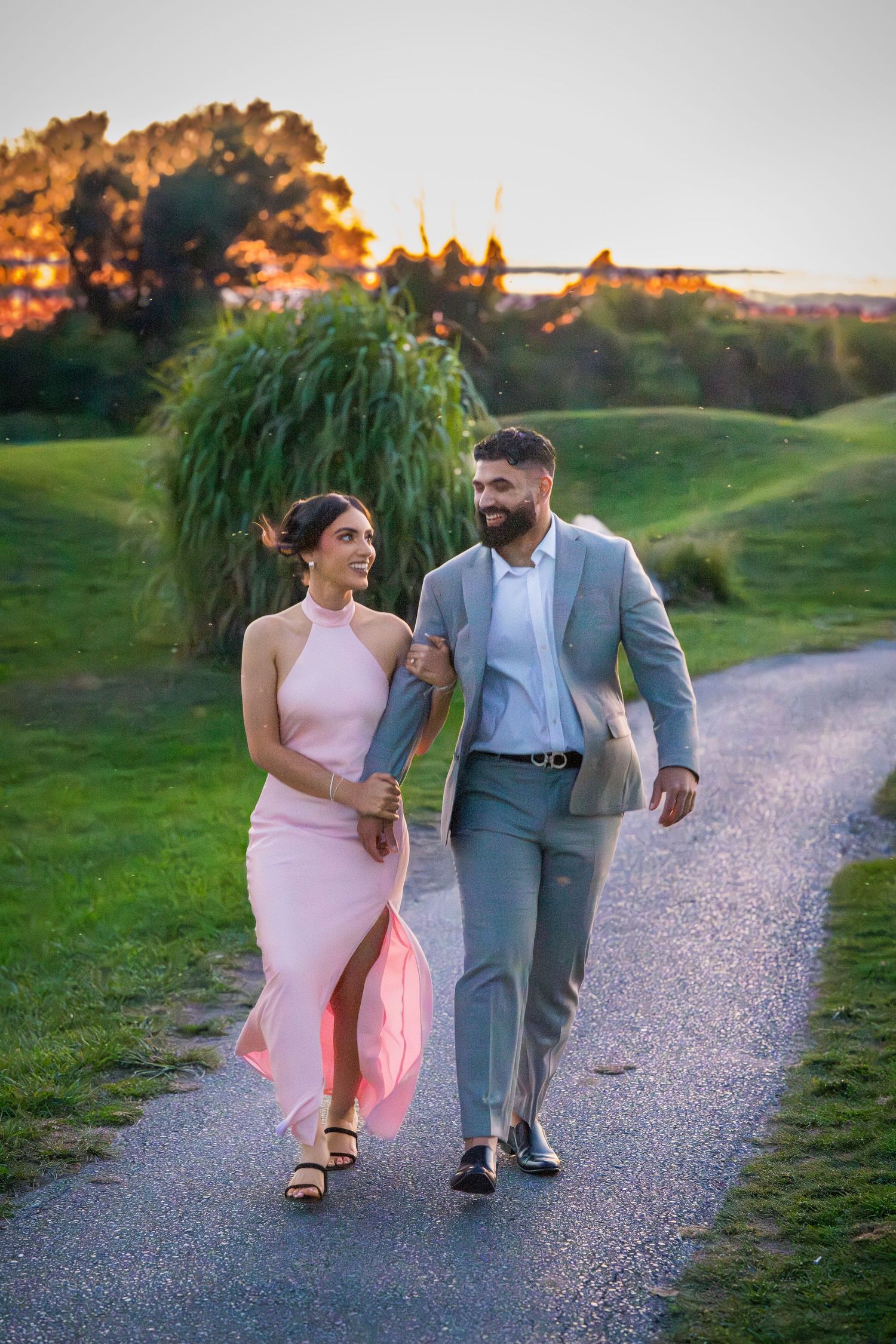 A couple walks arm in arm along a scenic gravel path during sunset.