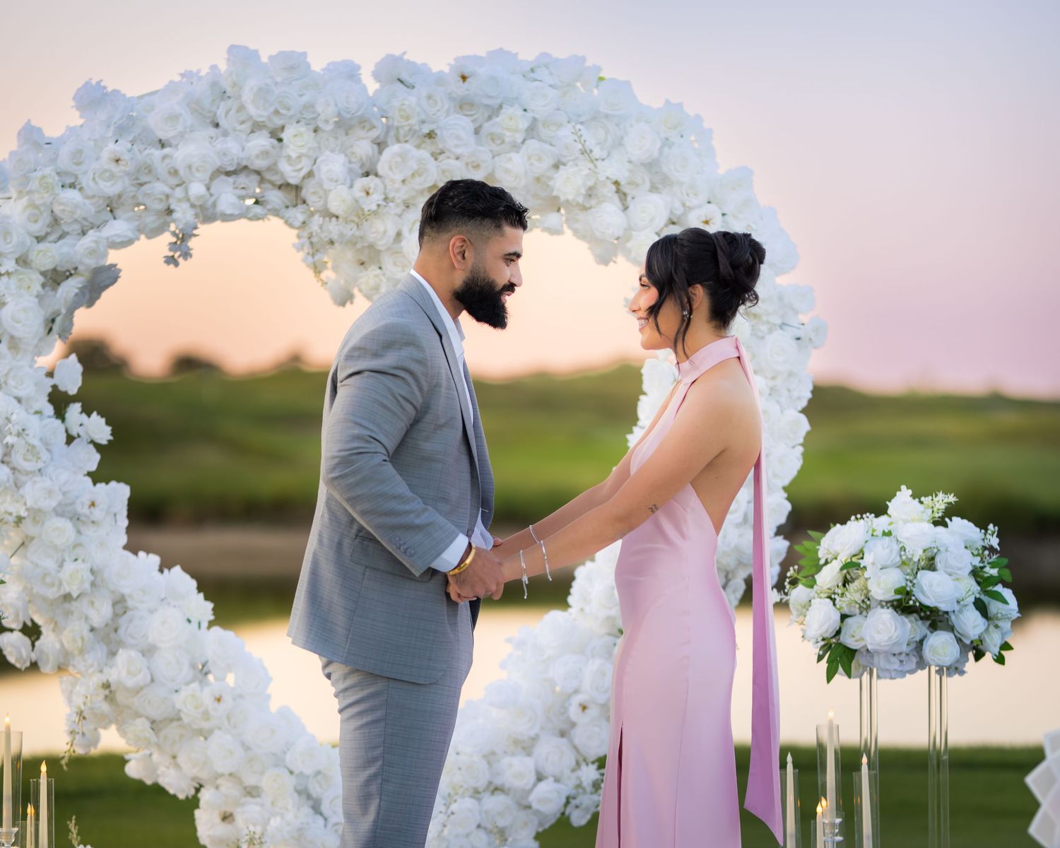 An elegant outdoor wedding setup with white floral arches and candles at sunset.