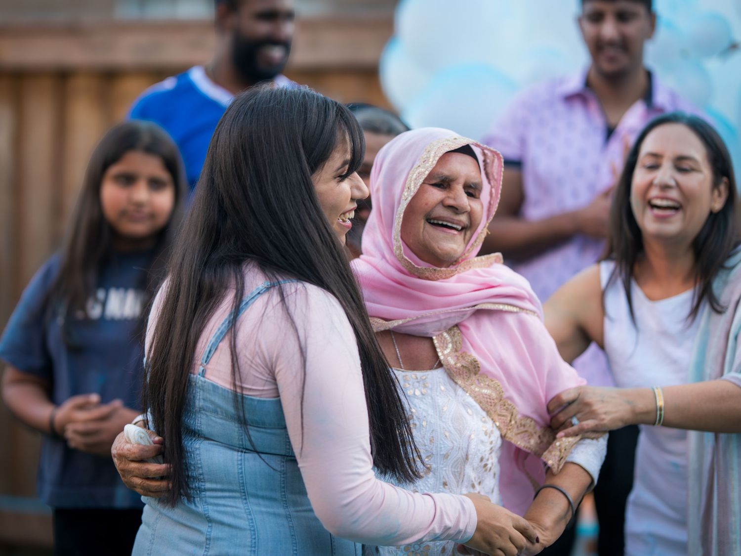 Women laughing and embracing at an outdoor gender reveal celebration with blue powder.