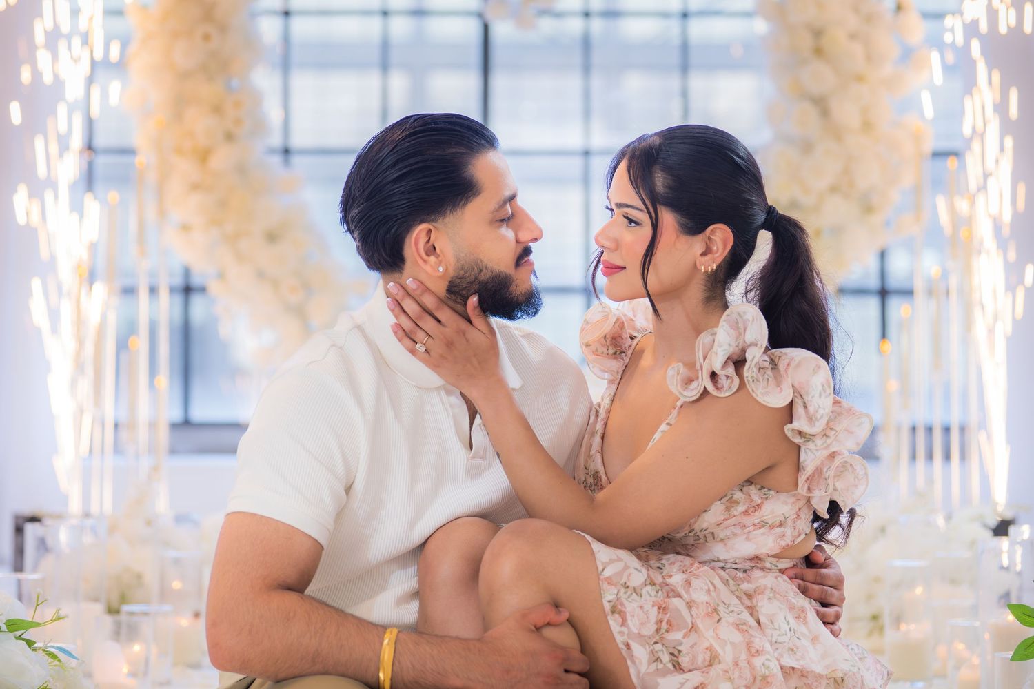 Couple sharing an intimate moment sitting on the floor in front of a beautiful white floral heart arch display.
