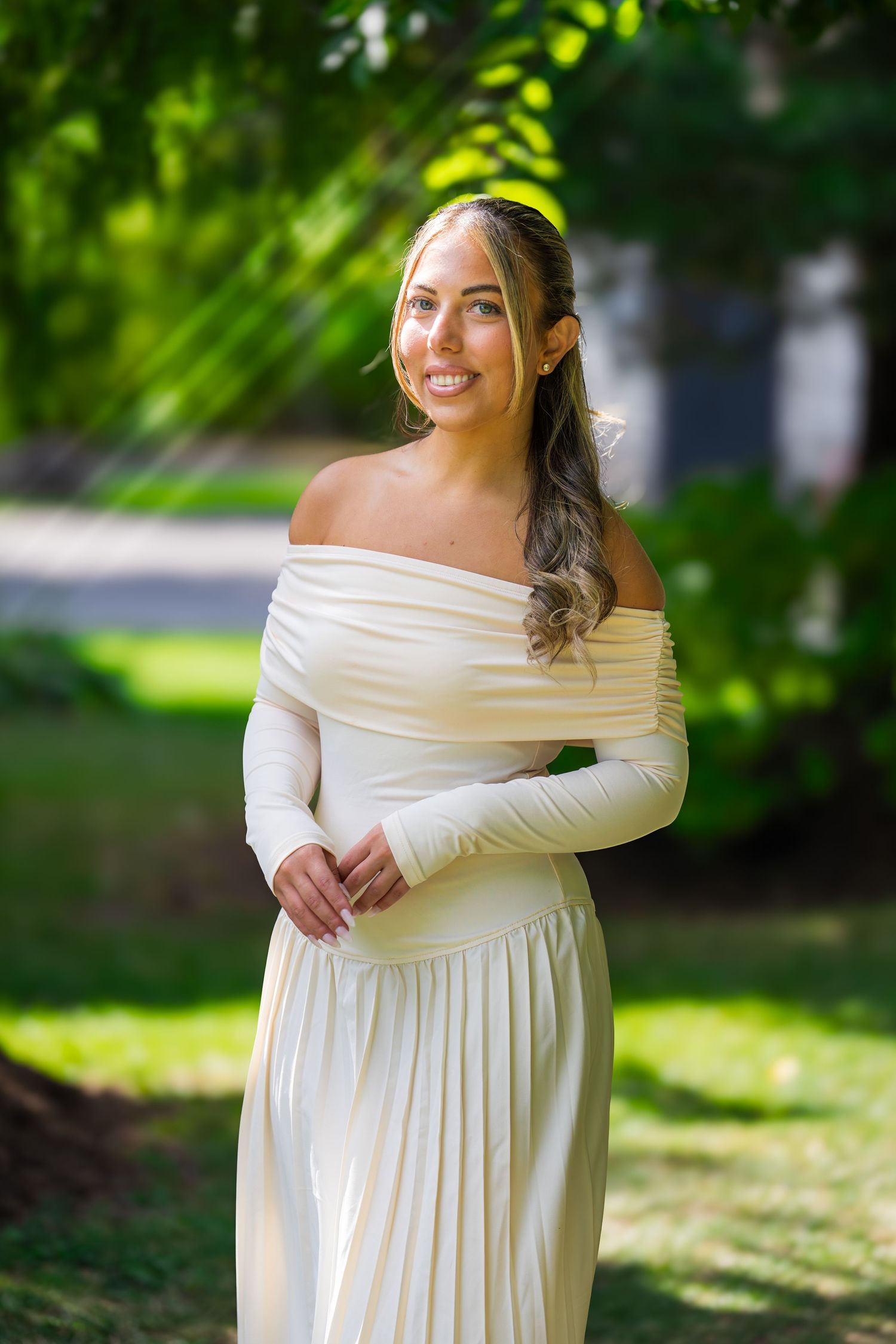 Elegant off-shoulder white dress photographed in natural outdoor setting.