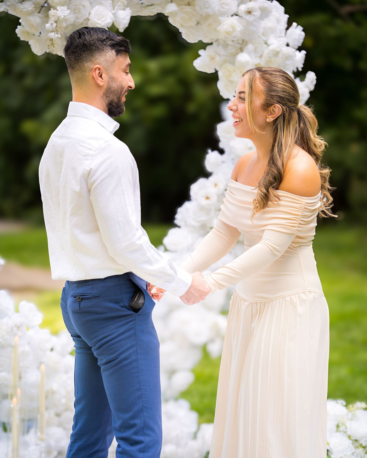A couple sharing an intimate moment under an elegant white floral arch during their outdoor wedding.