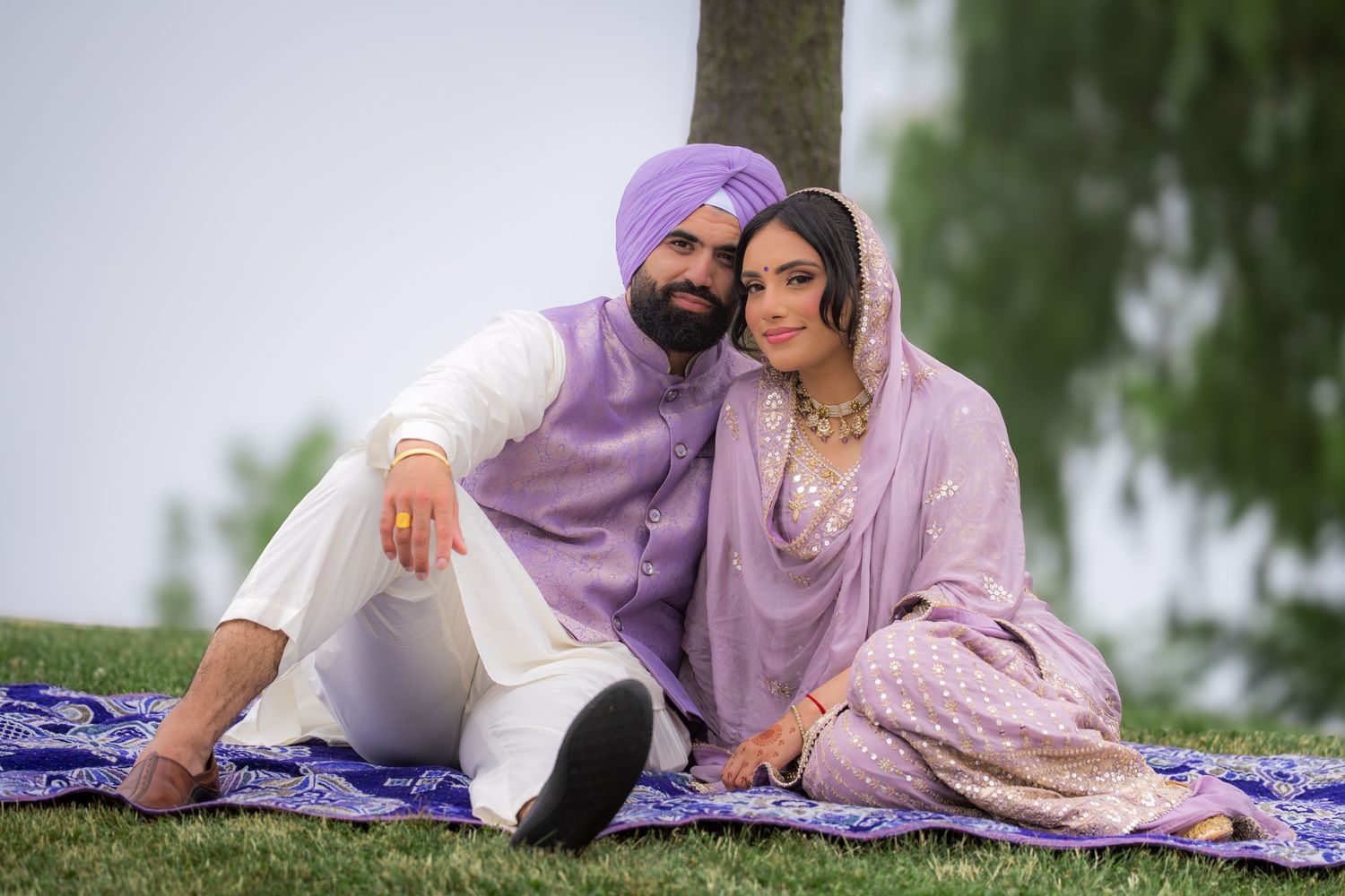 A couple in traditional Punjabi attire shares a romantic moment on a picnic blanket outdoors.