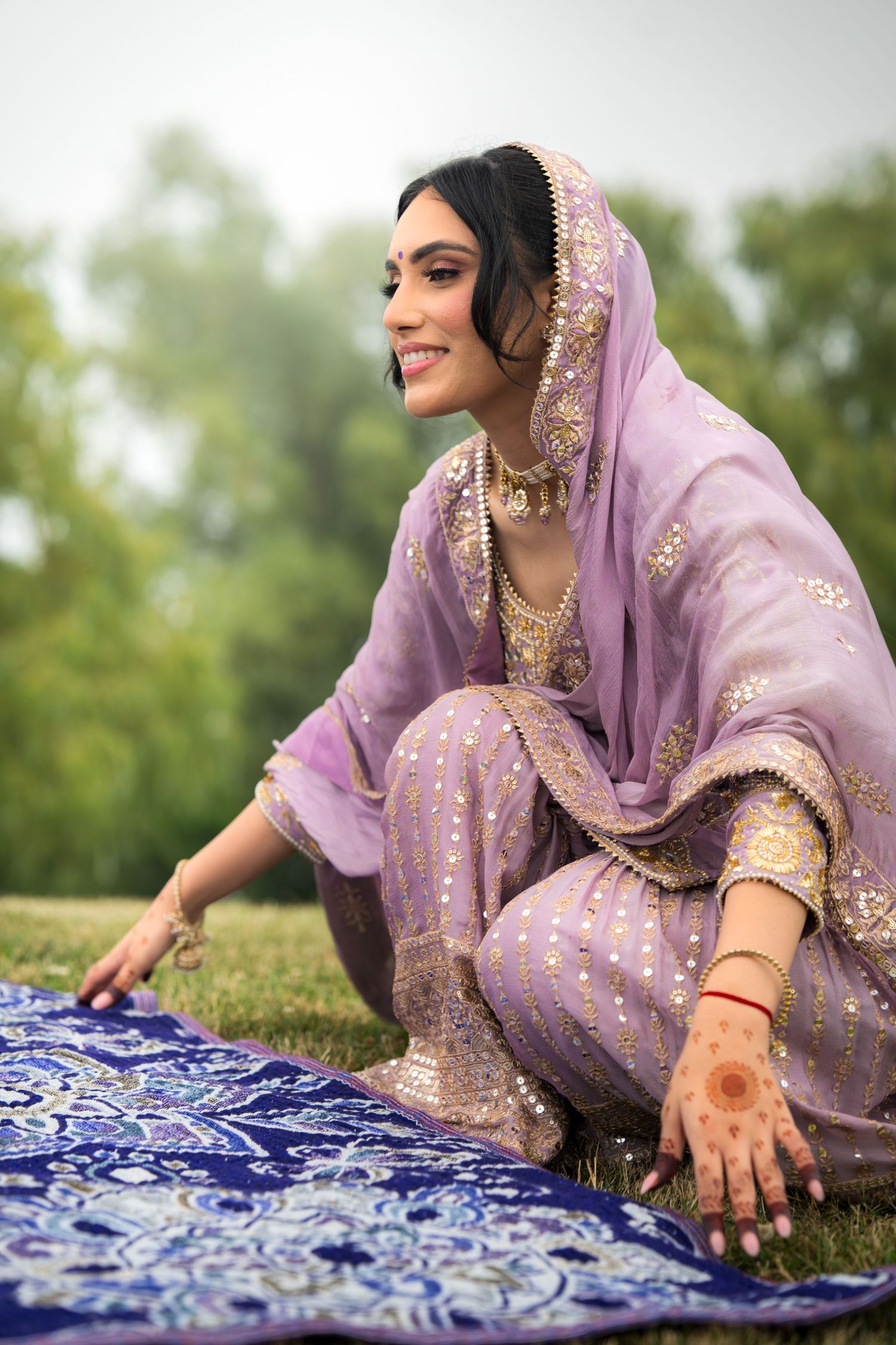 Lavender traditional dress with gold embroidery displayed against blue patterned fabric on grass.