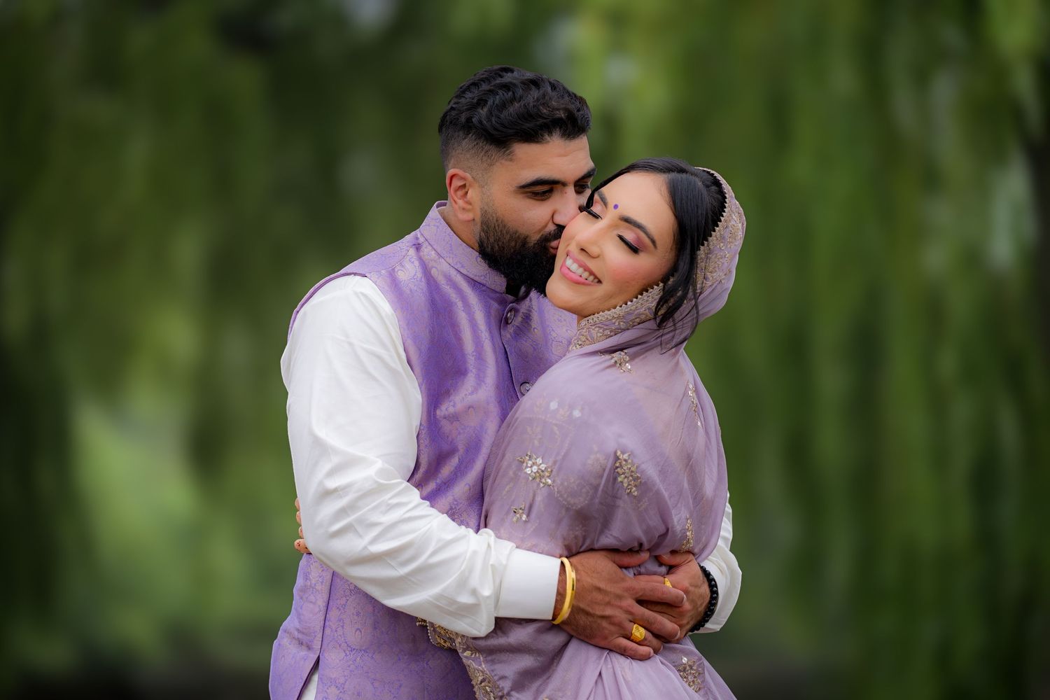 A couple in matching purple and white outfits embrace during an outdoor photoshoot.