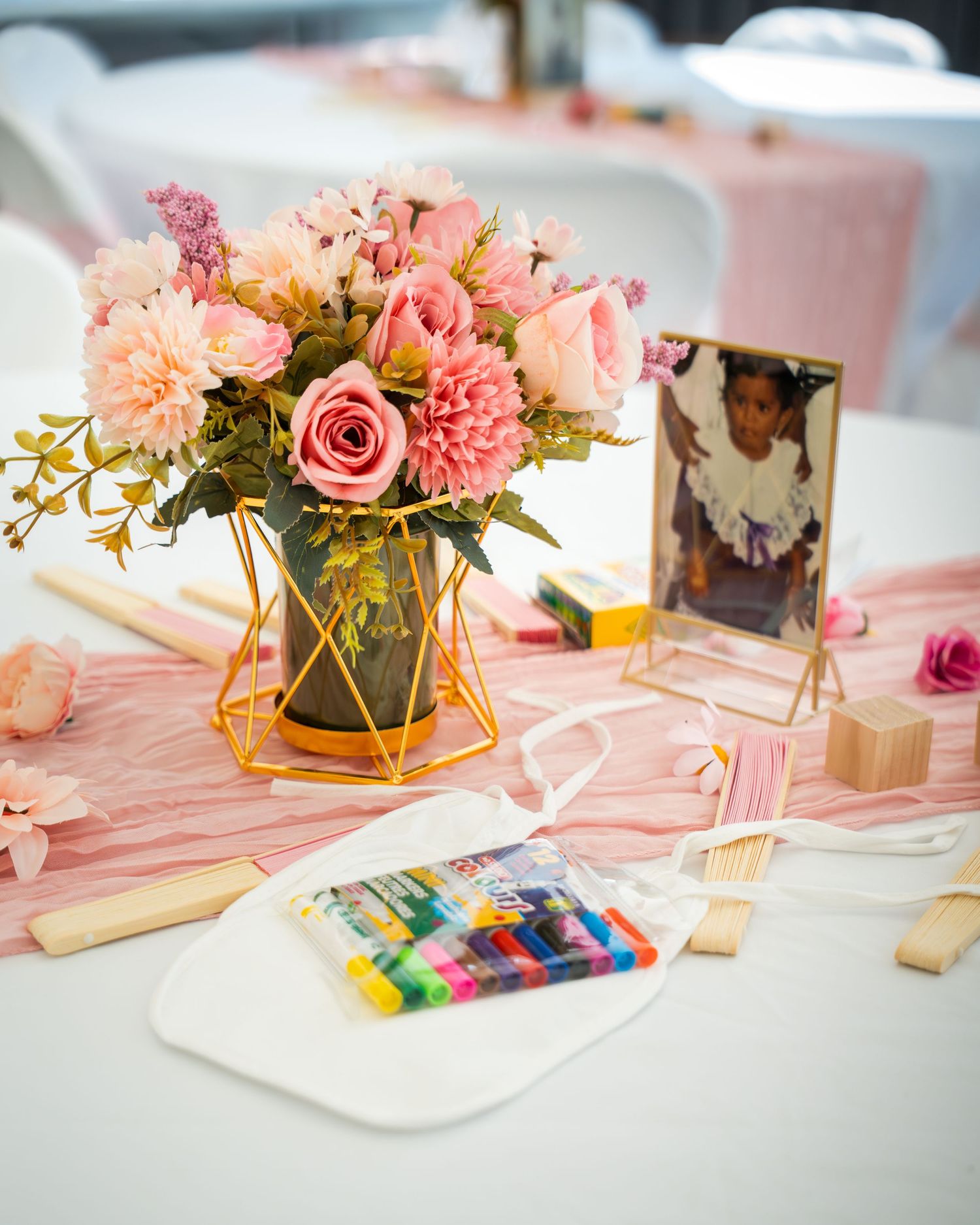 Pink table setting with floral centerpieces, gold accents, and craft supplies for a baby shower.