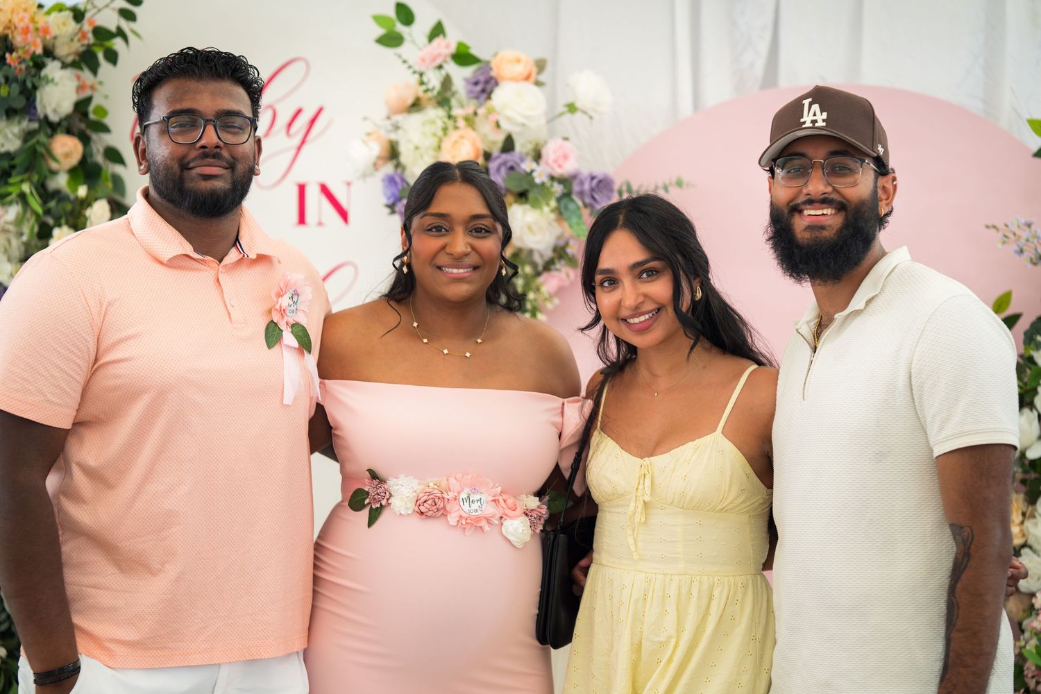 Celebration attendees posed together wearing coordinated pastel outfits against a floral backdrop.