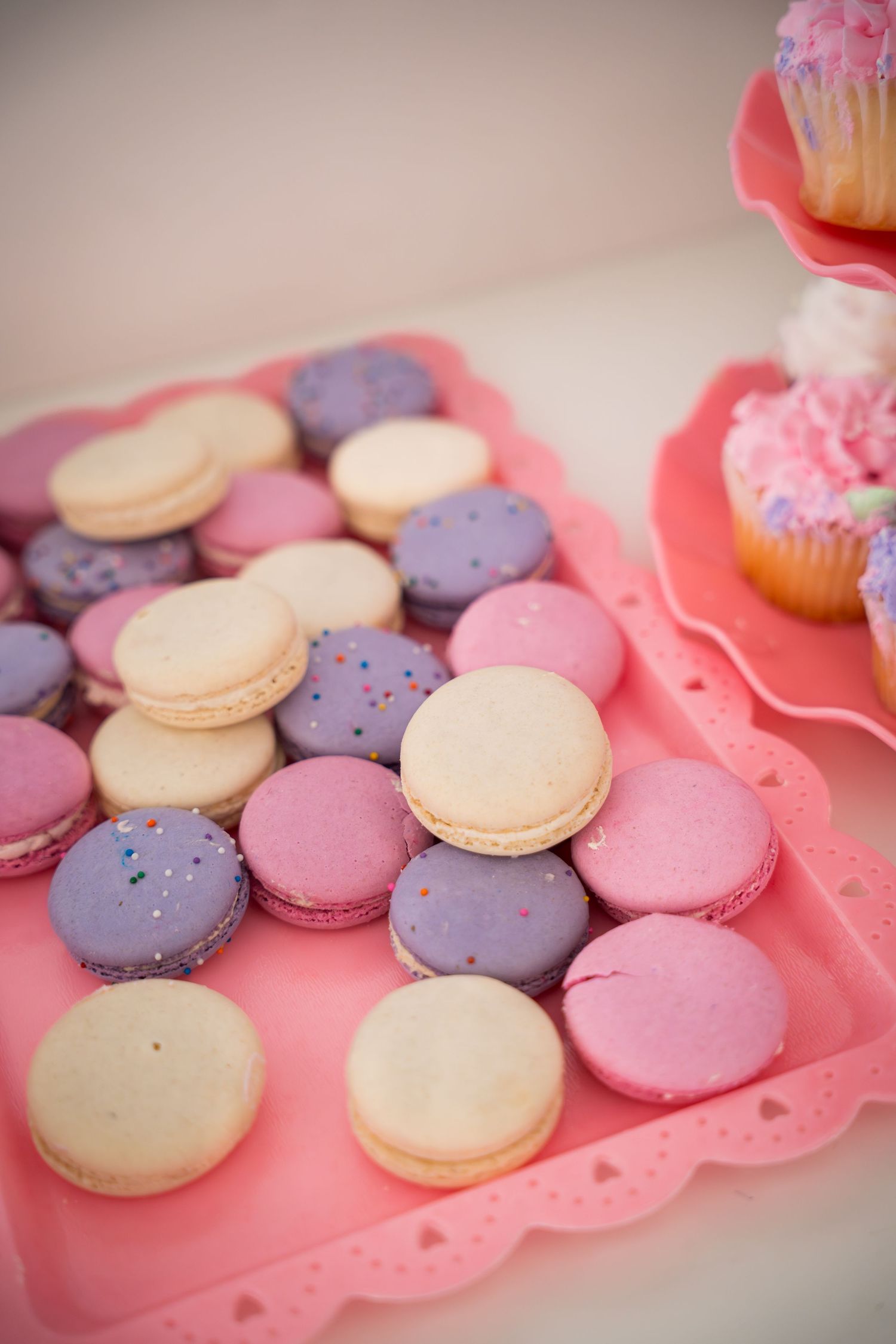Colorful macarons in pink, purple, and cream arranged on a scalloped pink serving tray.