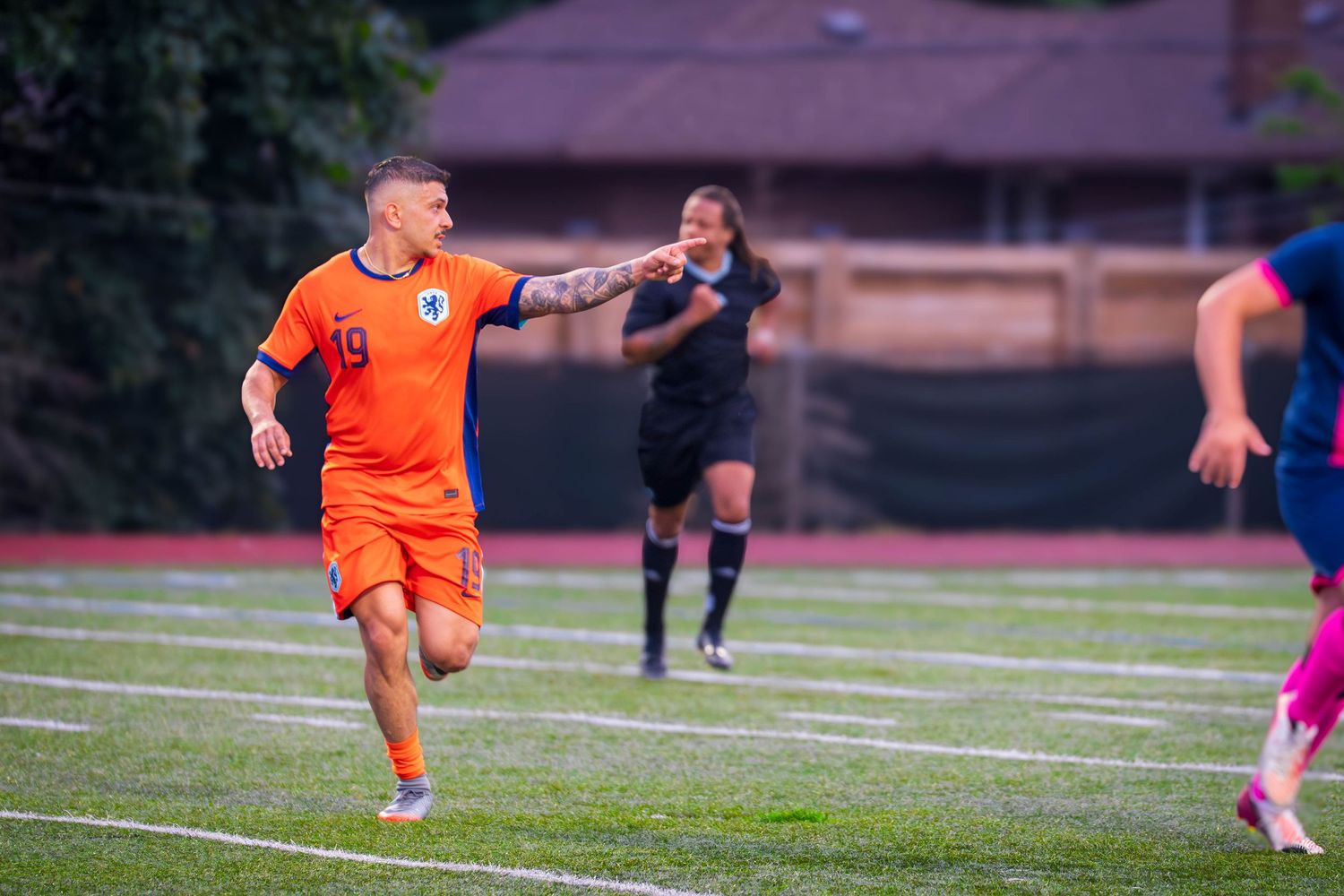 Soccer players in orange and navy uniforms compete on a grass playing field.