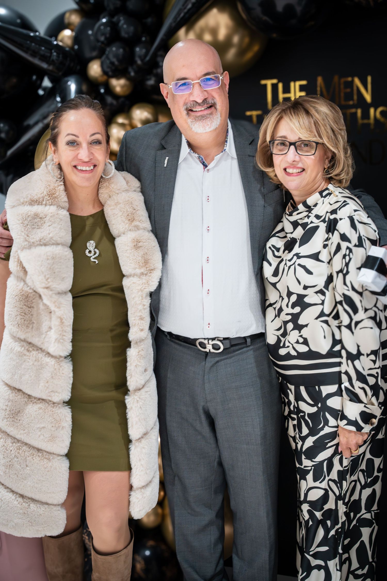 Three people posing together at formal event with gold balloon decorations.