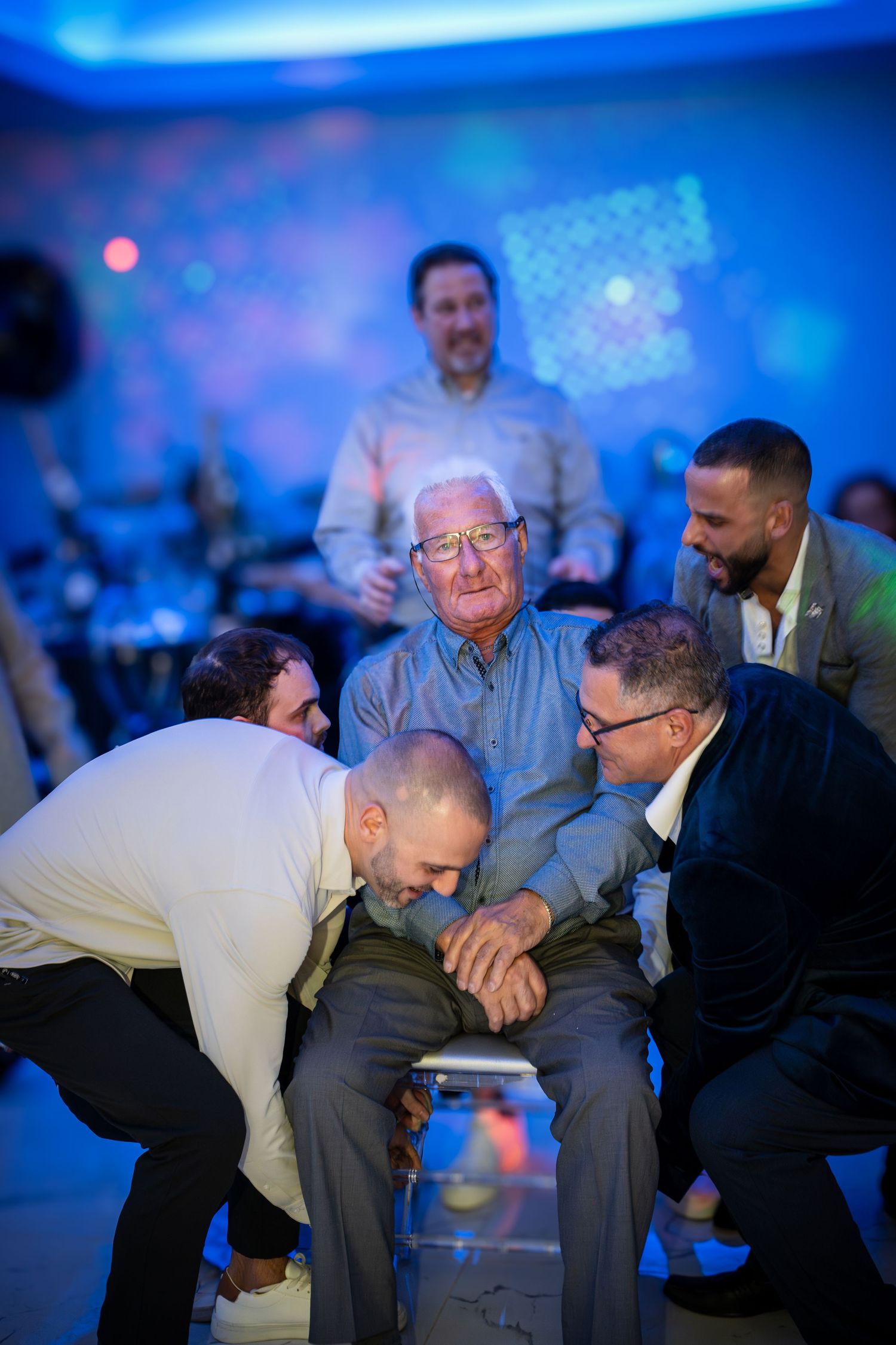 A group of men laughing together at an indoor event with blue ambient lighting.