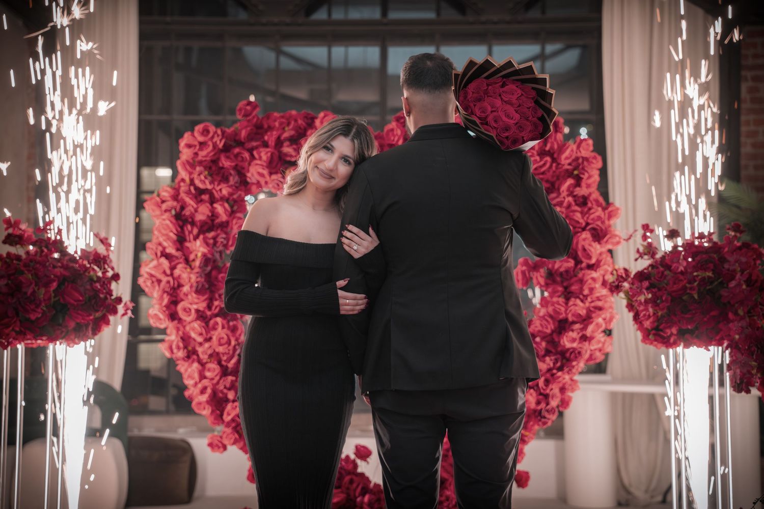 Romantic proposal setup with red rose wall and white sparklers creating a magical atmosphere.