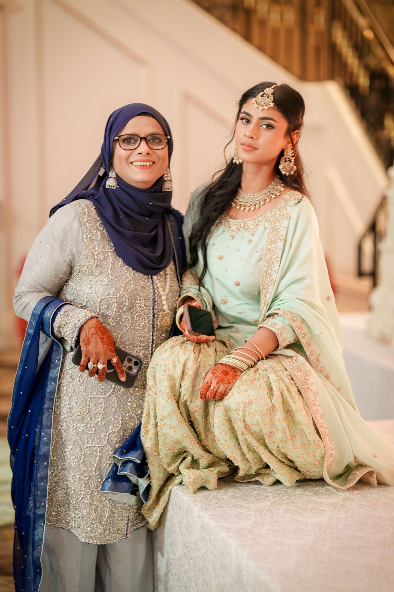 Wedding celebration showing two women in traditional South Asian attire with henna adorned hands.