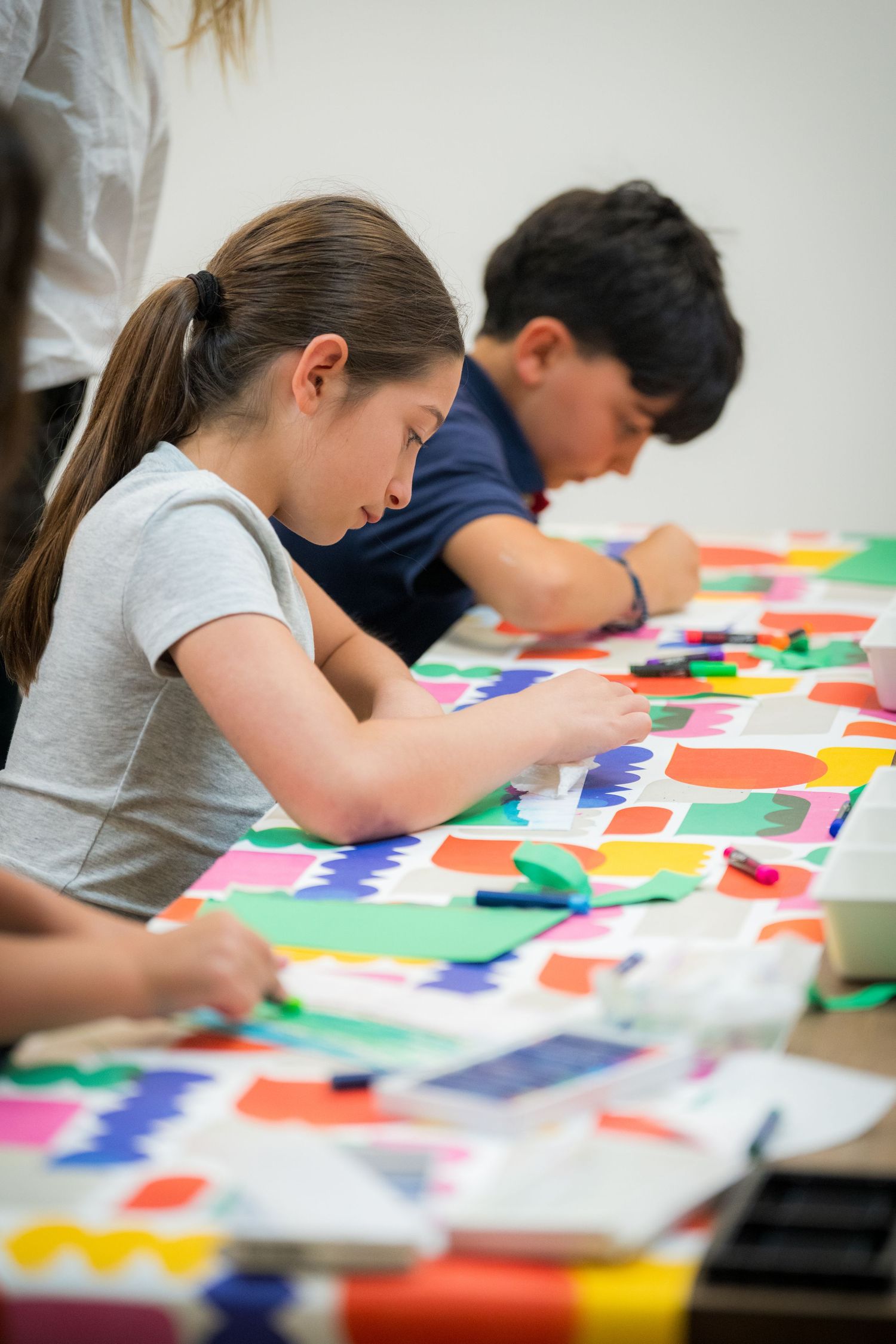 Kids concentrate on cutting and arranging colorful paper shapes in an art class.