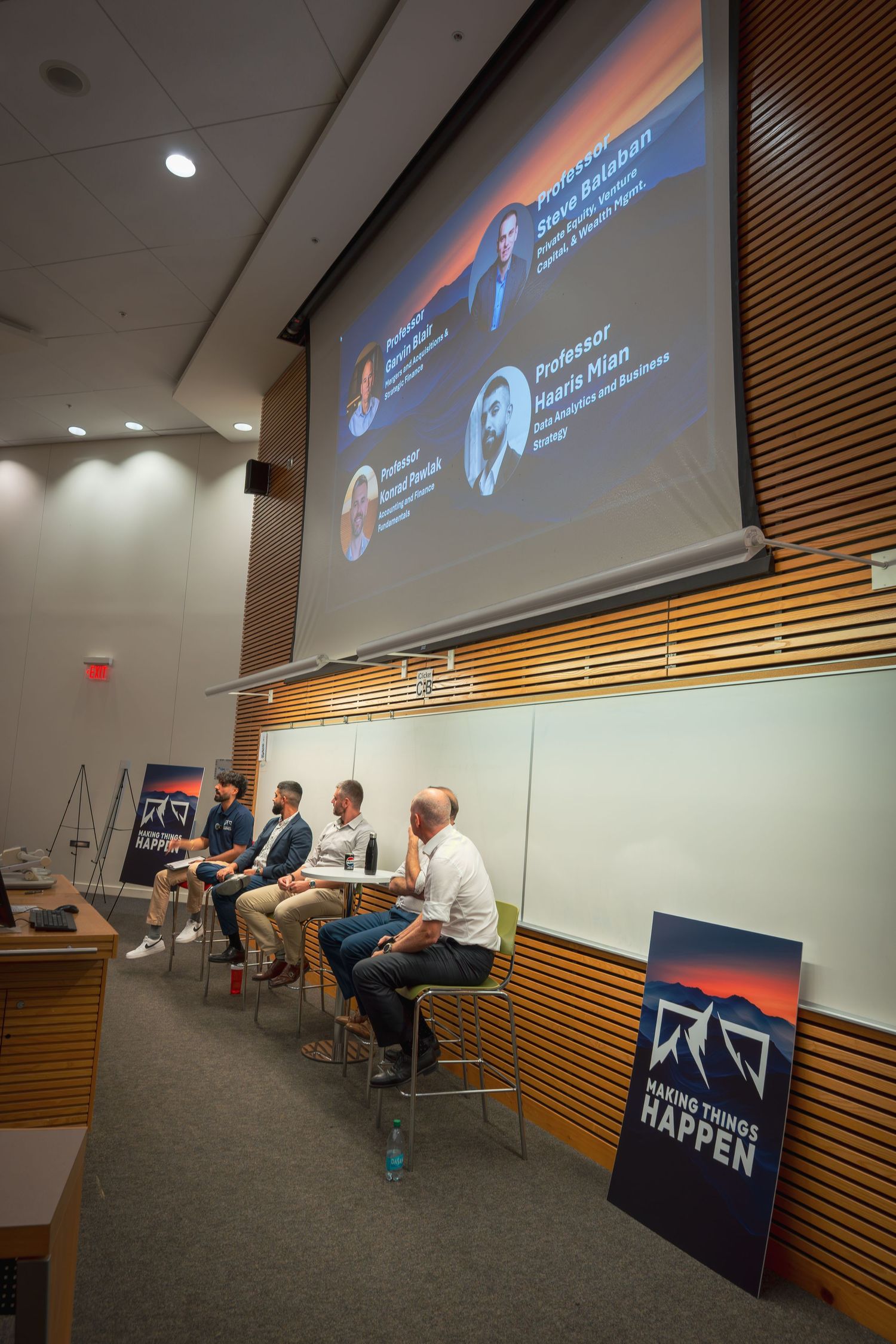 Panel discussion taking place in a modern conference room with wood paneling and projected presentation display.