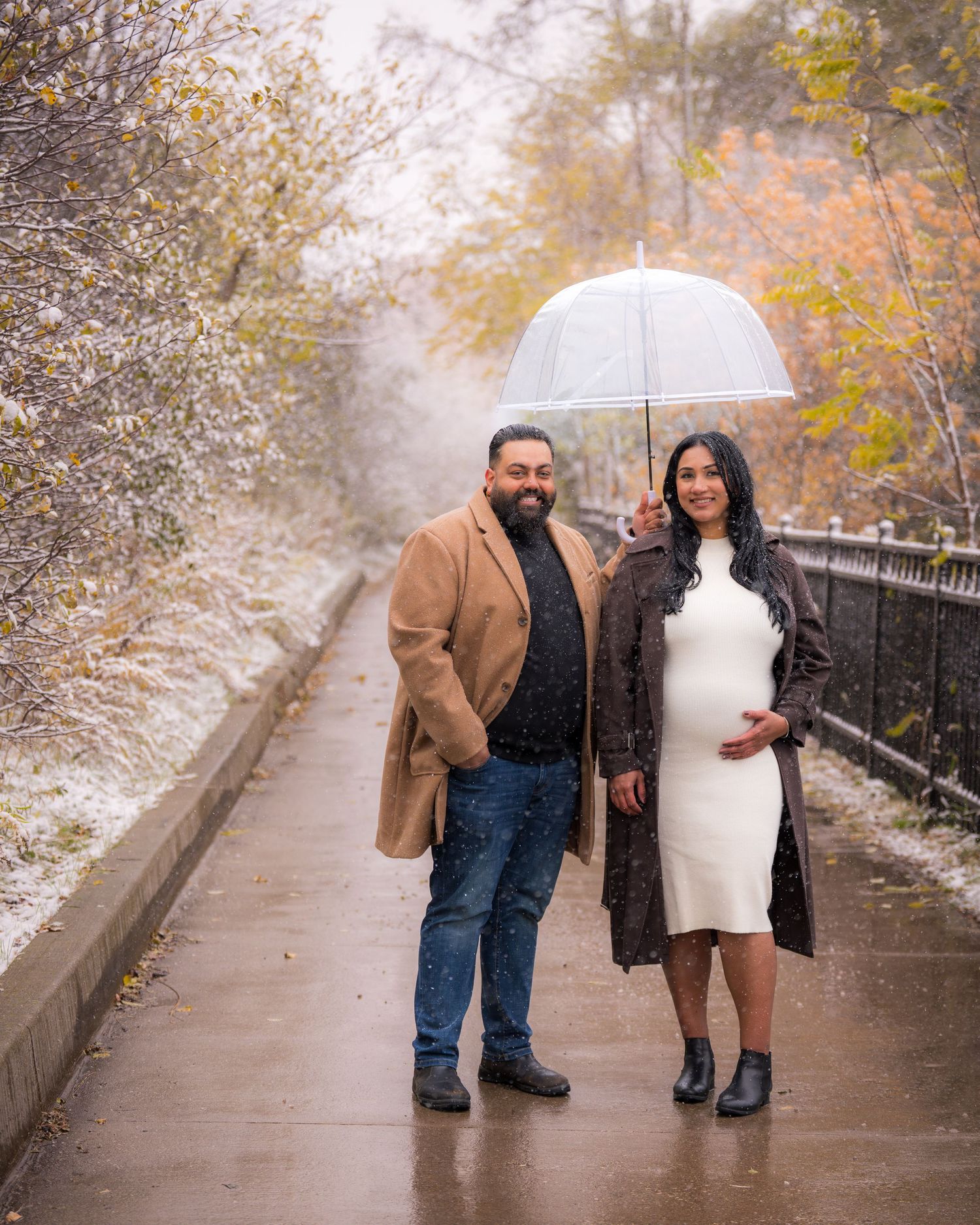 A couple walks along a snowy path during an autumn engagement photoshoot.