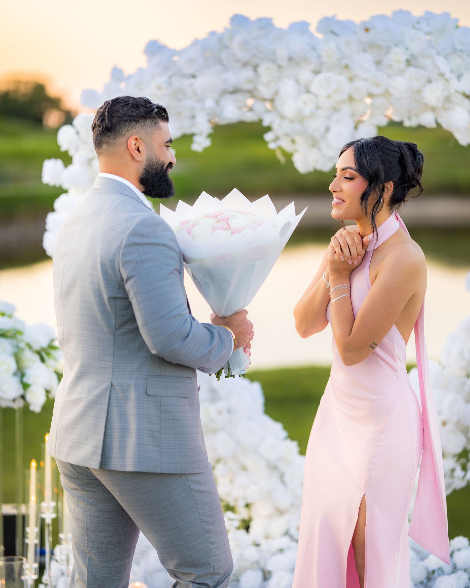 Emotional proposal moment under an elegant white flower arch during golden hour.