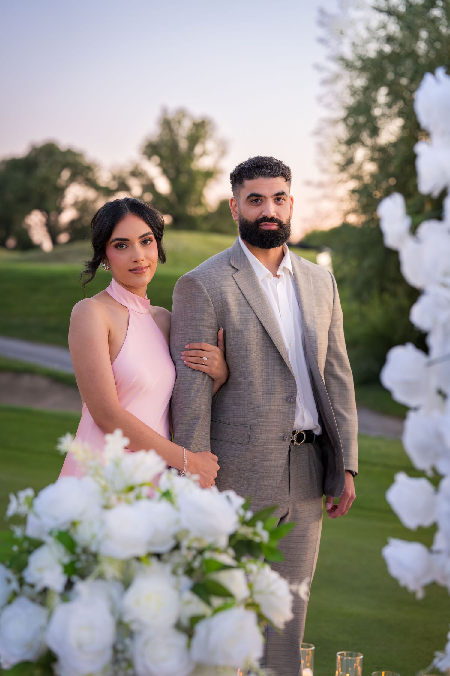 Outdoor photoshoot with couple near white balloon arch and floral arrangements.