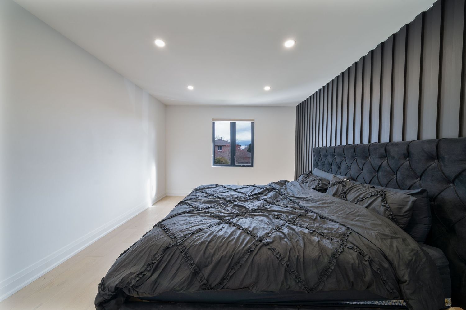 A modern bedroom features dark vertical wall panels, recessed lighting, and a plush black bedding set against white walls.