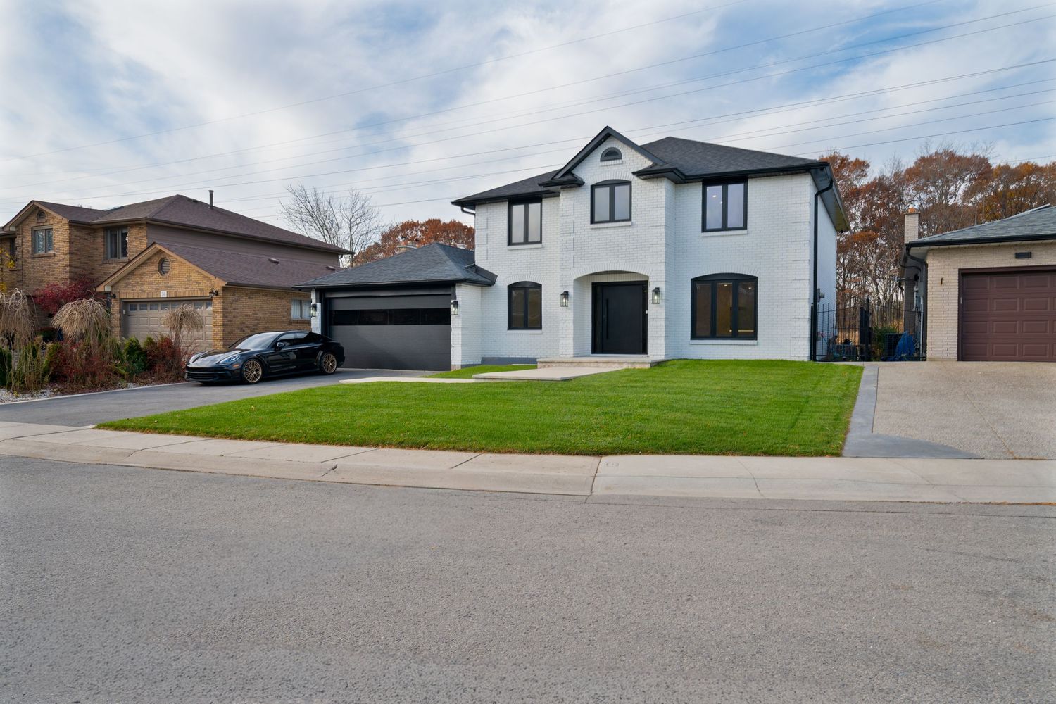 Modern residential homes line a quiet suburban street with well-maintained lawns and driveways on a cloudy day.