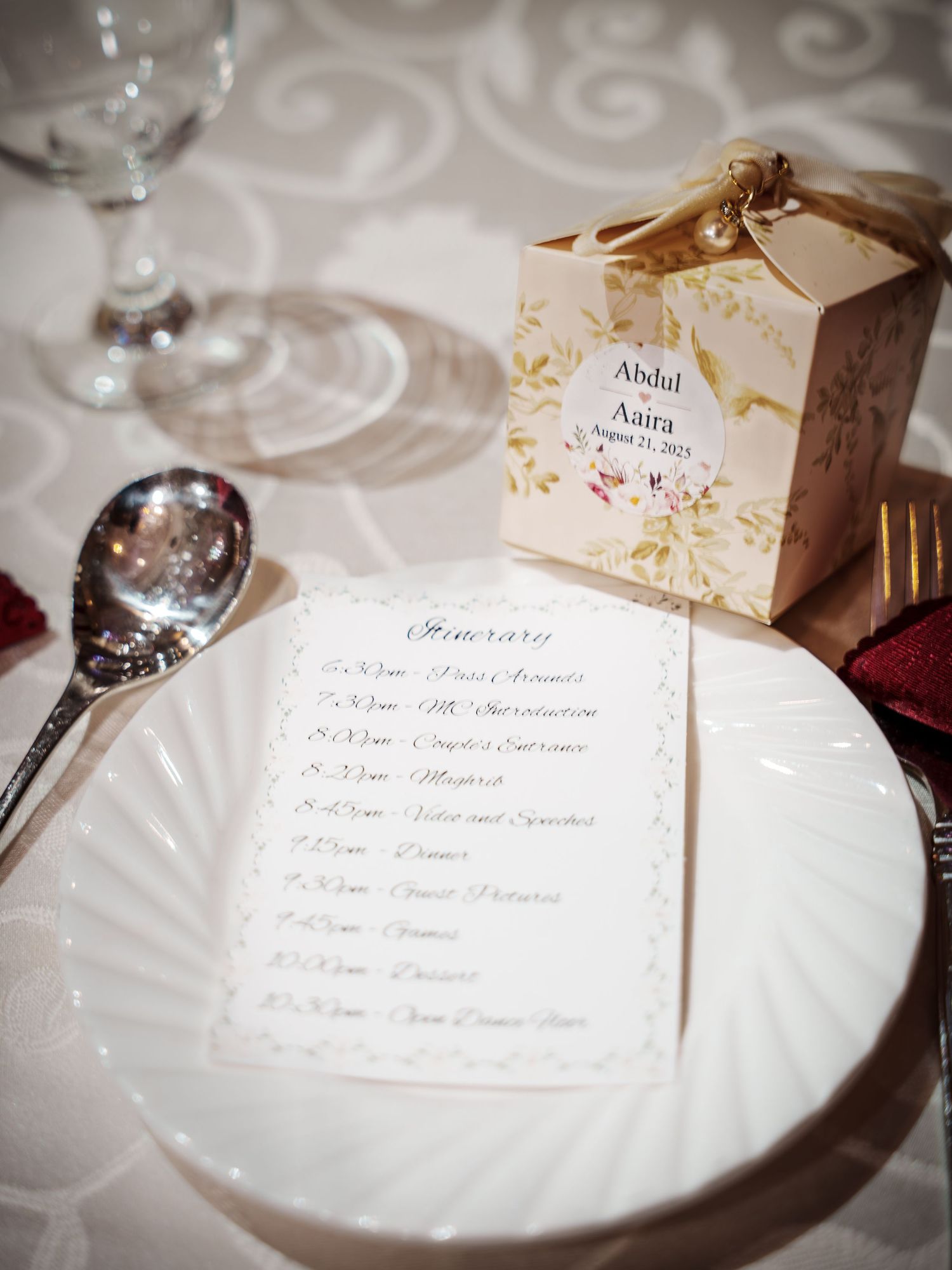 Wedding reception place setting with menu card and decorative favor box on white tablecloth.