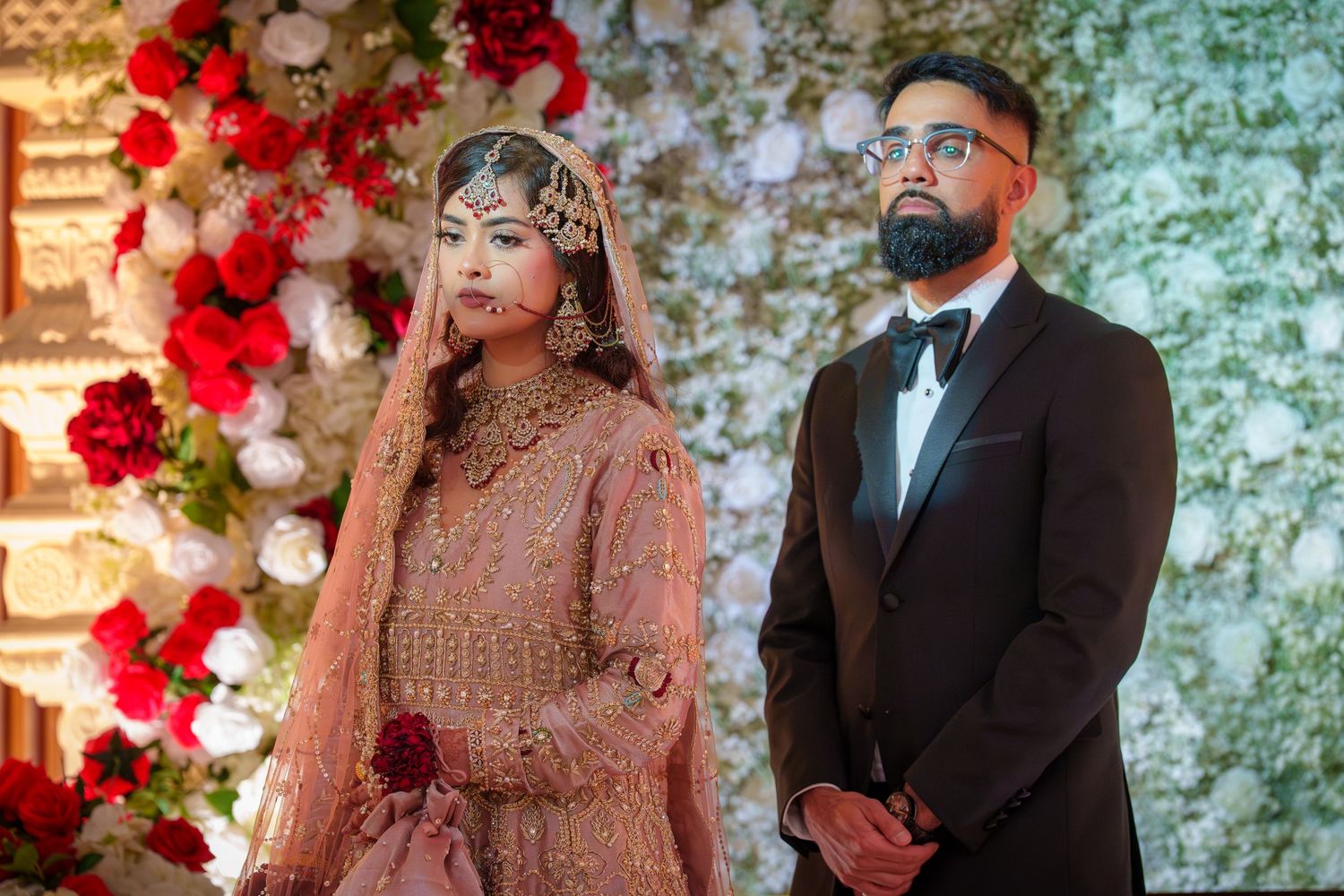 Wedding ceremony setup with red floral arch and couple in traditional South Asian formal attire.
