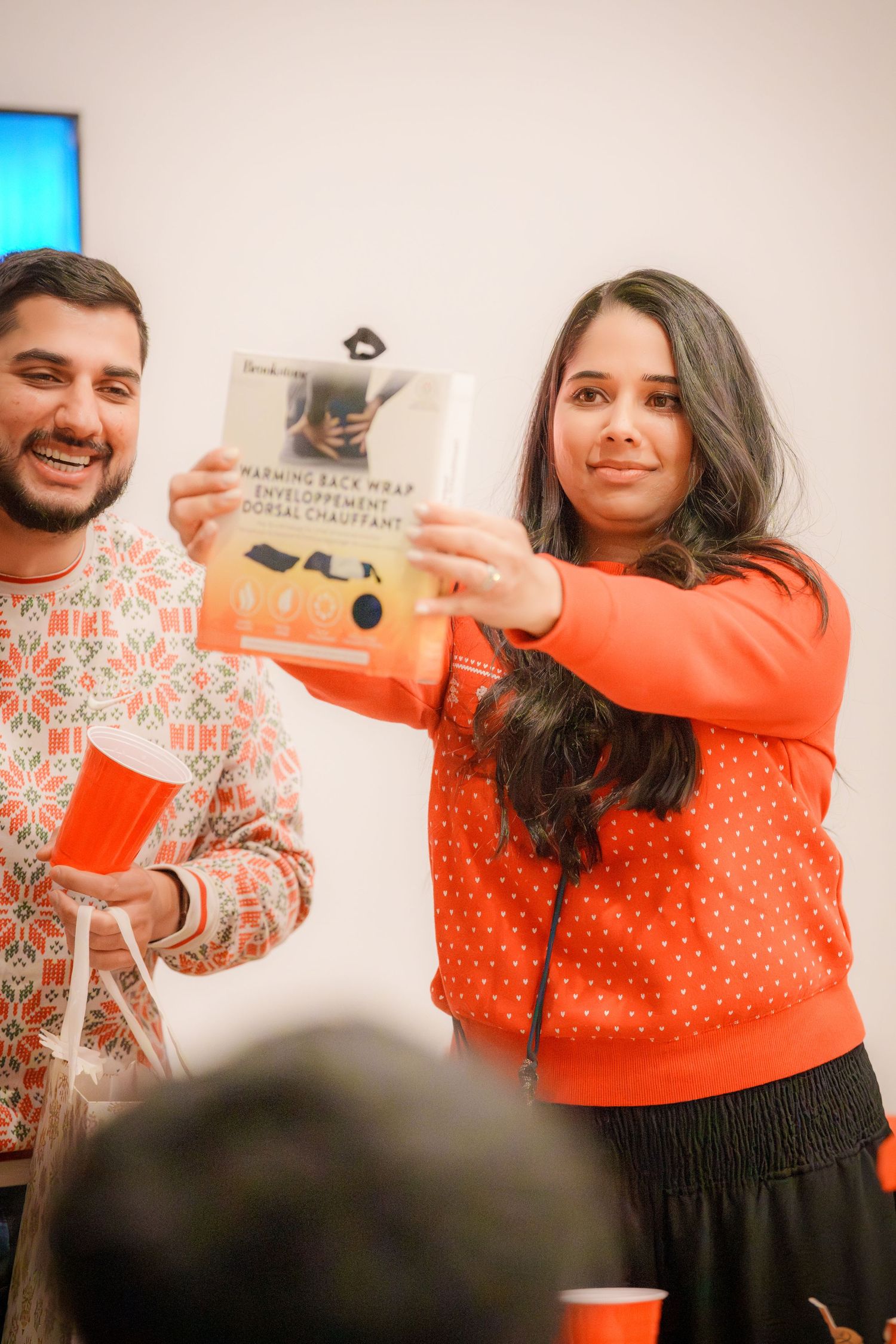 Person in orange sweater showing books at a holiday gathering.