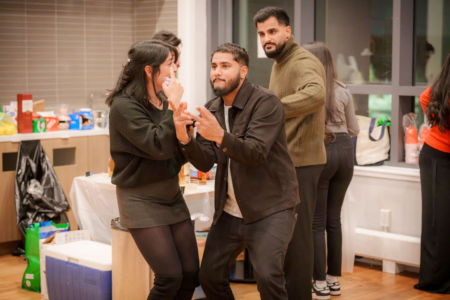 People interacting at an indoor social gathering with windows visible in background.